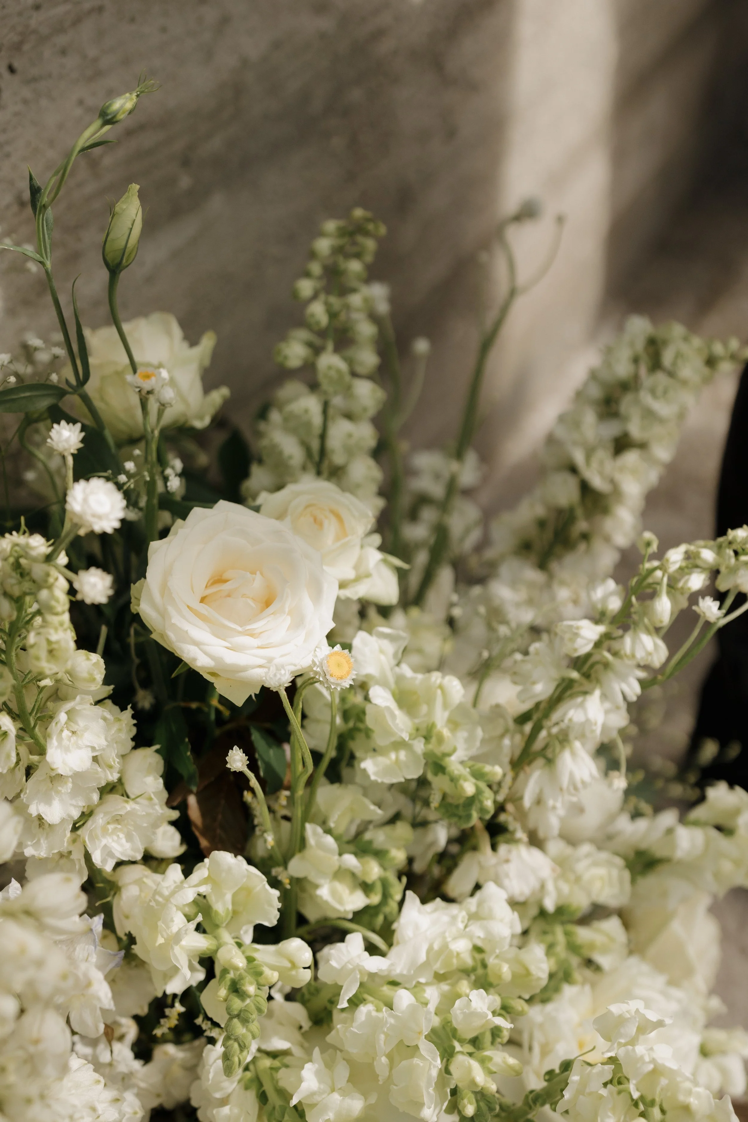 A bouquet of white roses, daisies, and other white flowers against a beige background.