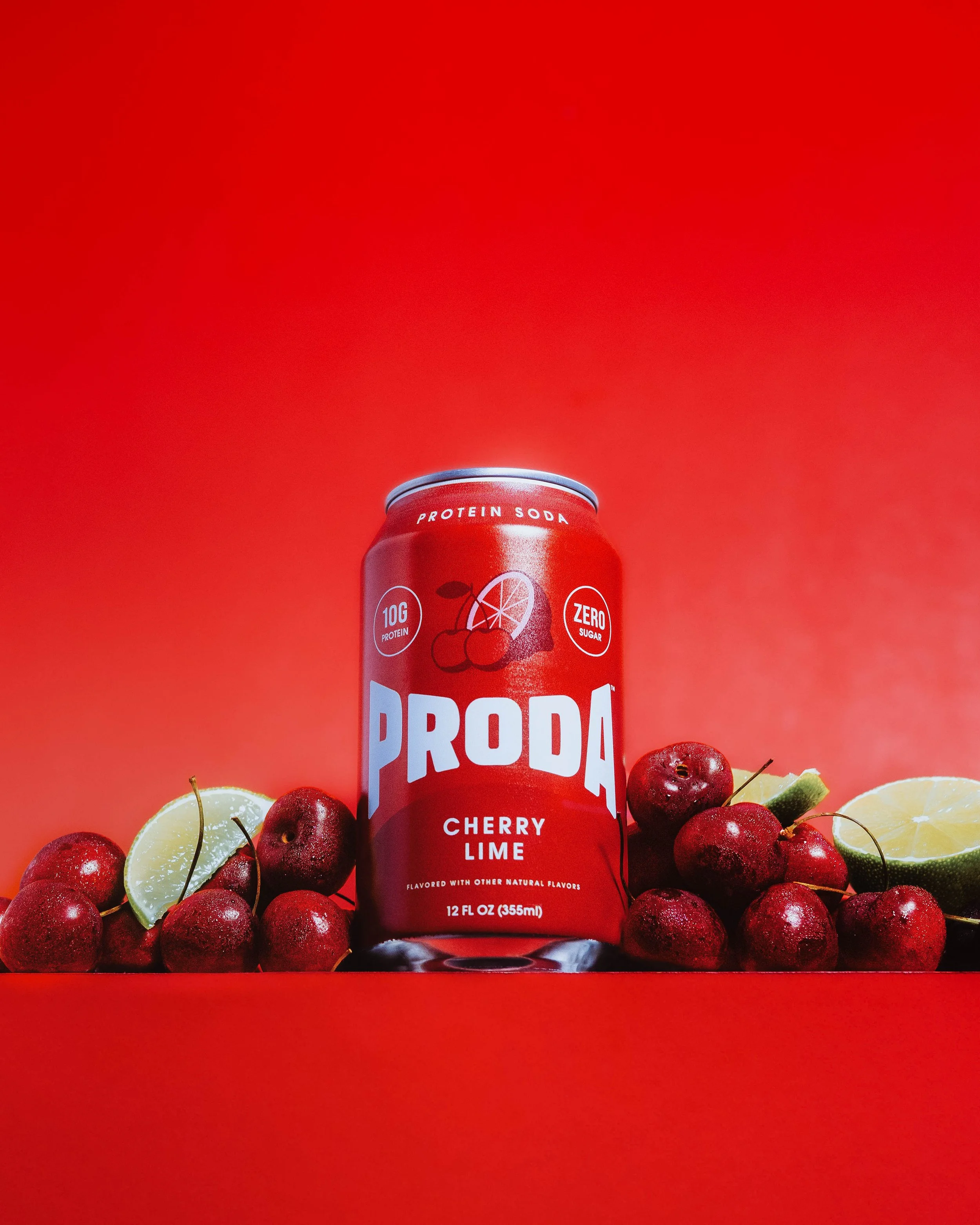 A can of Proda cherry lime flavored sparkling water surrounded by cherries, lemon slices, and lime slices on a red background.