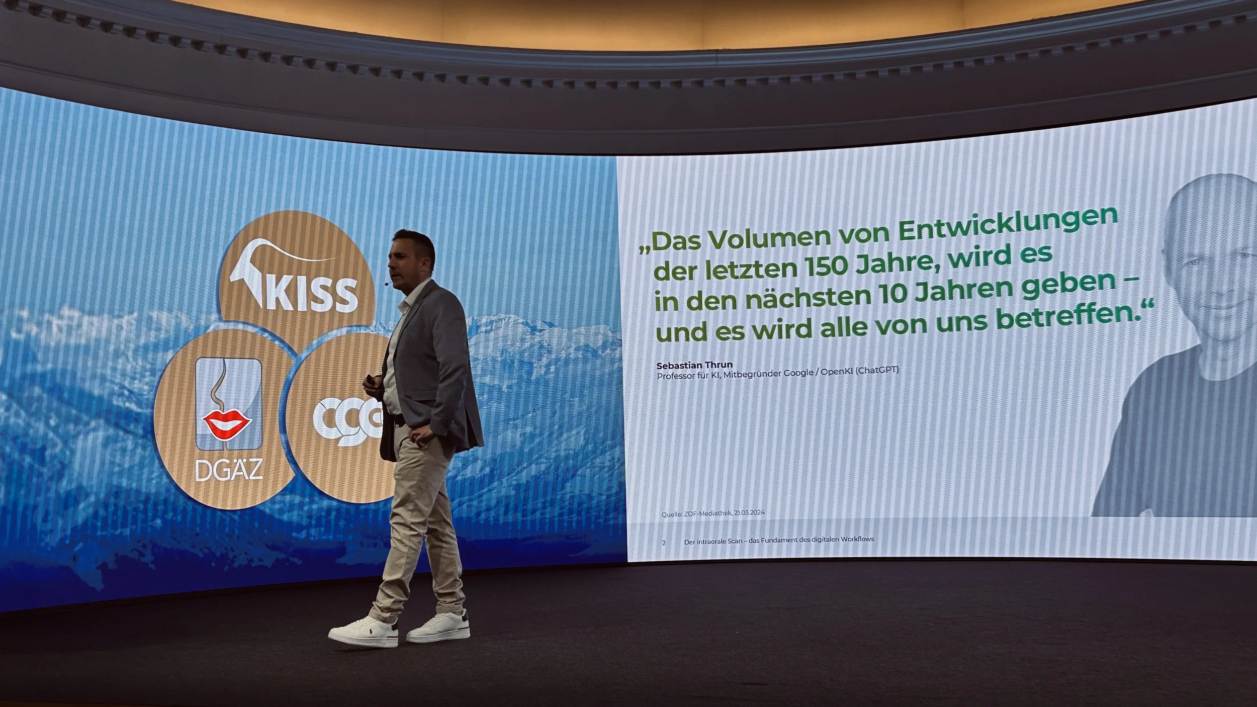 Vizepräsident Fabian Lorenz bei dem DGÄZ-Kongress in Kitzbühel , auf dem ein Zitat in Deutsch steht. Der Bildschirm zeigt auch mehrere Symbole und Logos. Der Hintergrund ist dunkel, der Raum hat eine moderne Atmosphäre.