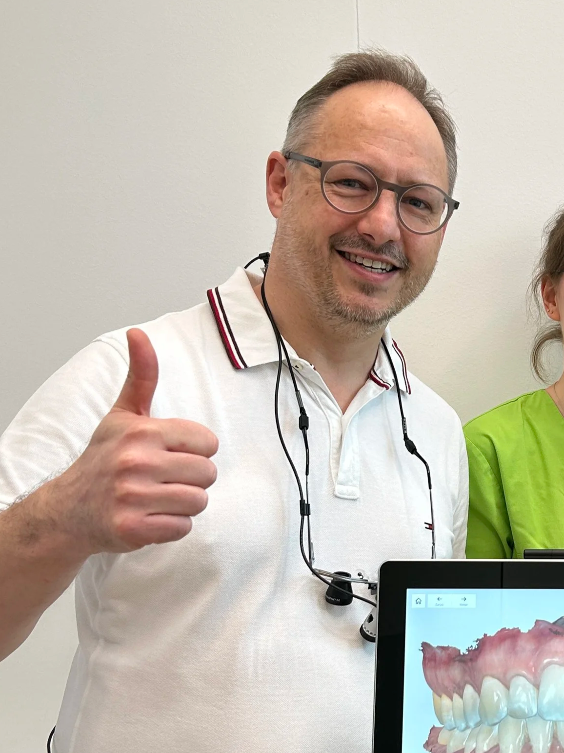 Mann mit Brille und weißen Hemd, der einem Daumen nach oben zeigt, neben einem digitalen Zahnmodell