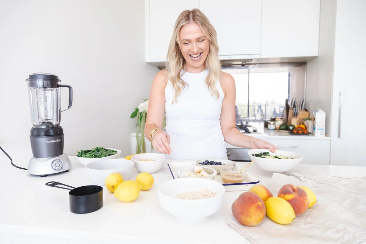 Georgina Waugh in a kitchen with a blender and bowls of spinach, oats, blueberries and fruit
