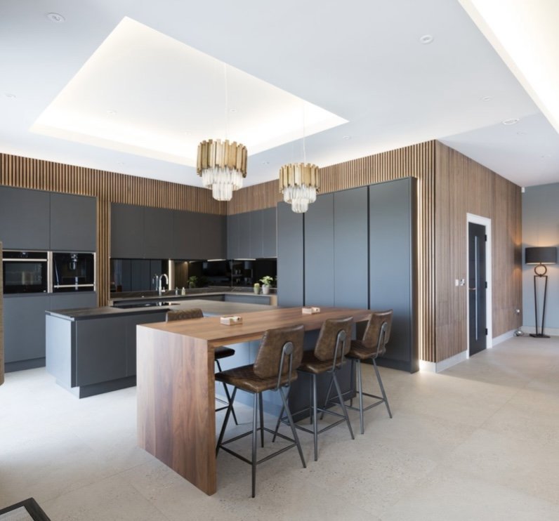 Modern Handless kitchen finished in Matt Graphite, Solid Dekton worktops, mirror back-splash, Walnut acoustic wall paneling, solid wood breakfast bar with a matching waterfall leg