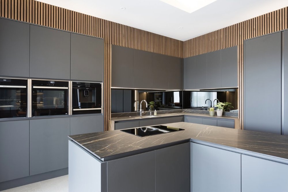 Modern Handless kitchen finished in Matt Graphite, Solid Dekton worktops, mirror back-splash, Walnut acoustic wall paneling, Bora downdraft hob on the island with eye level Neff single oven, combi oven, warming drawer and a coffee machine