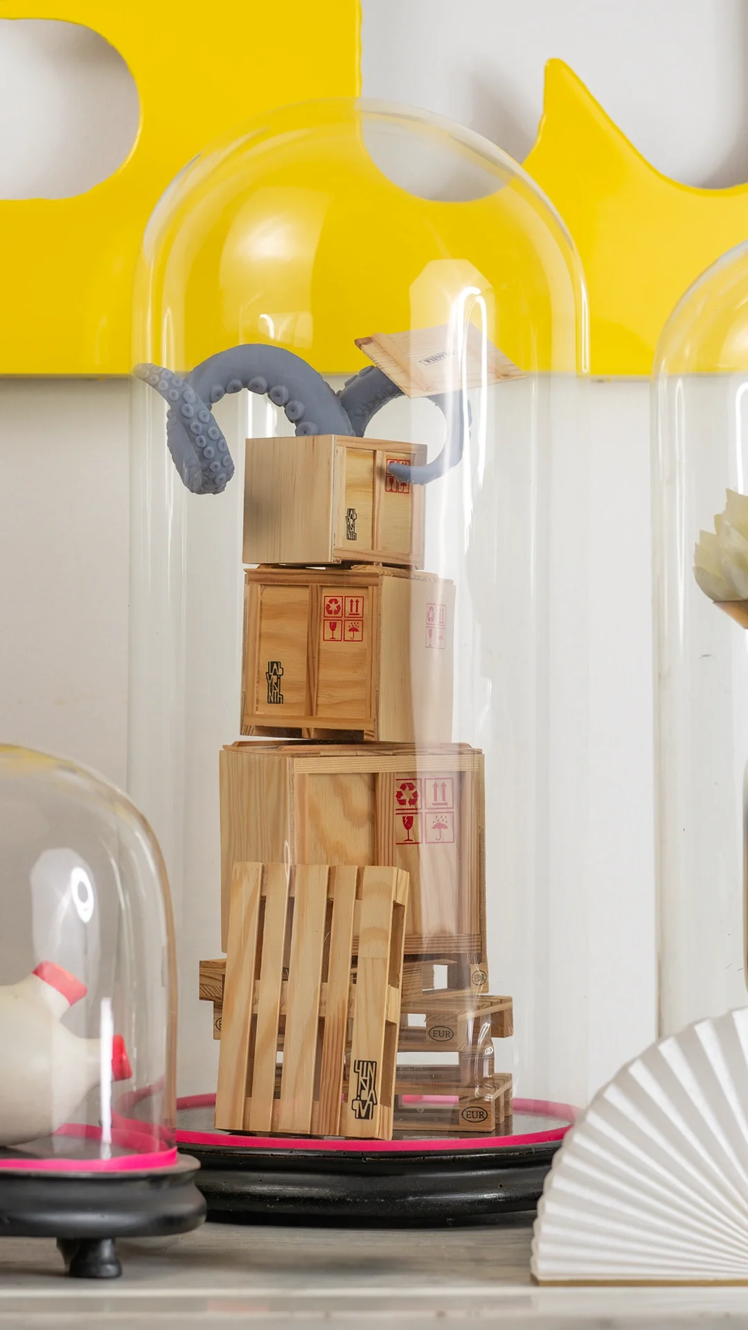 Überraschungsgäste — Close-up auf einen Glasdom, in dem aus einem Stapel Miniatur-Cargo-Kisten zwei Krakenarme platzen. Wehe dem, der …