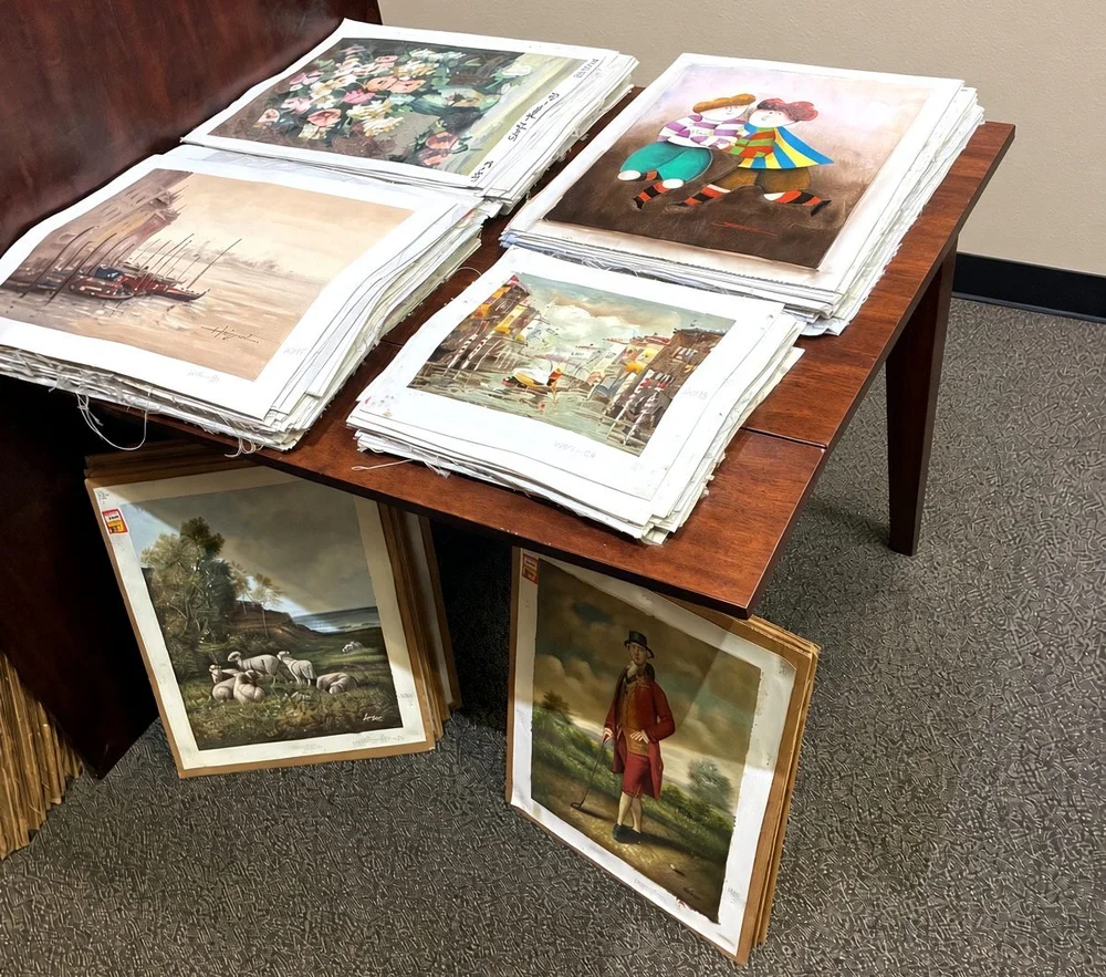Stacks of small unframed hand-painted paintings of flowers, children and harbor scenes on a table