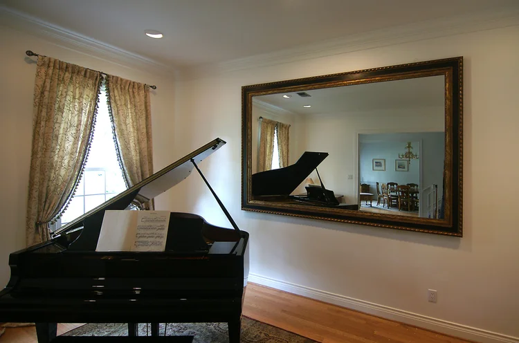 Large gold framed mirror in a living room beside a grand piano