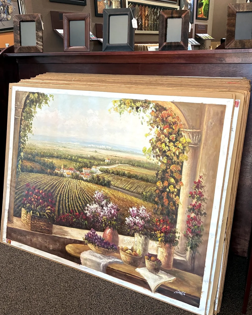 Large hand-painted Tuscany vineyard painting leaning in a browsing bin above leather photo frames