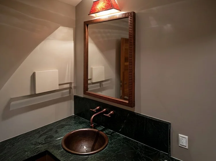 Custom wood framed bathroom mirror above a copper vessel sink