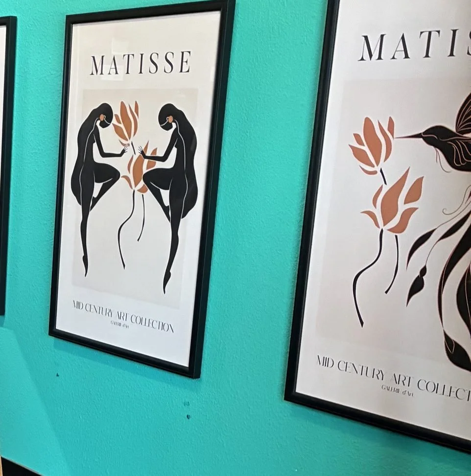 Framed art posters hang on a turquoise wall at The Frame Gallery in San Antonio