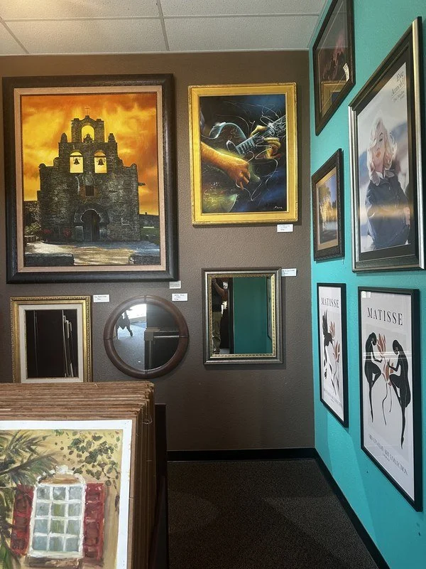 Showroom wall at The Frame Gallery in San Antonio with a framed mission painting, mirrors and framed posters