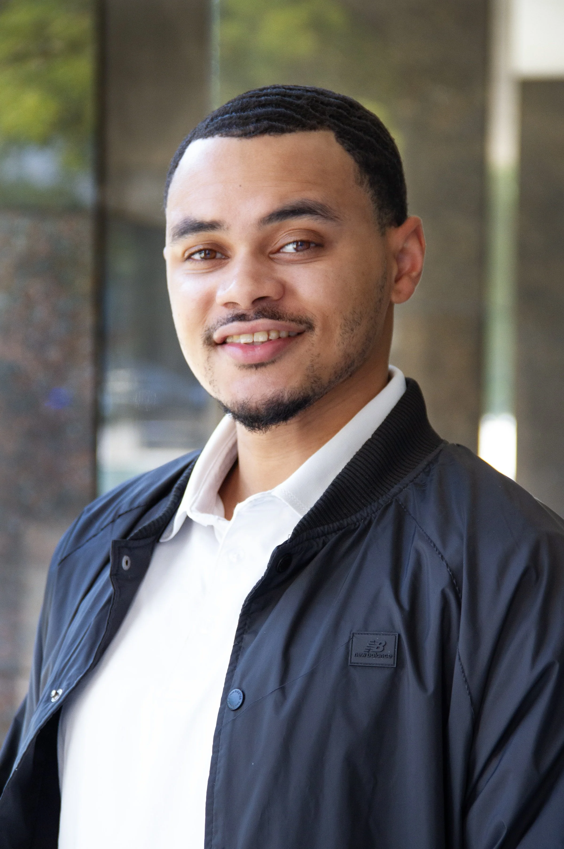 headshot of man with short dark hair, which colored polo shirt and navy jacket