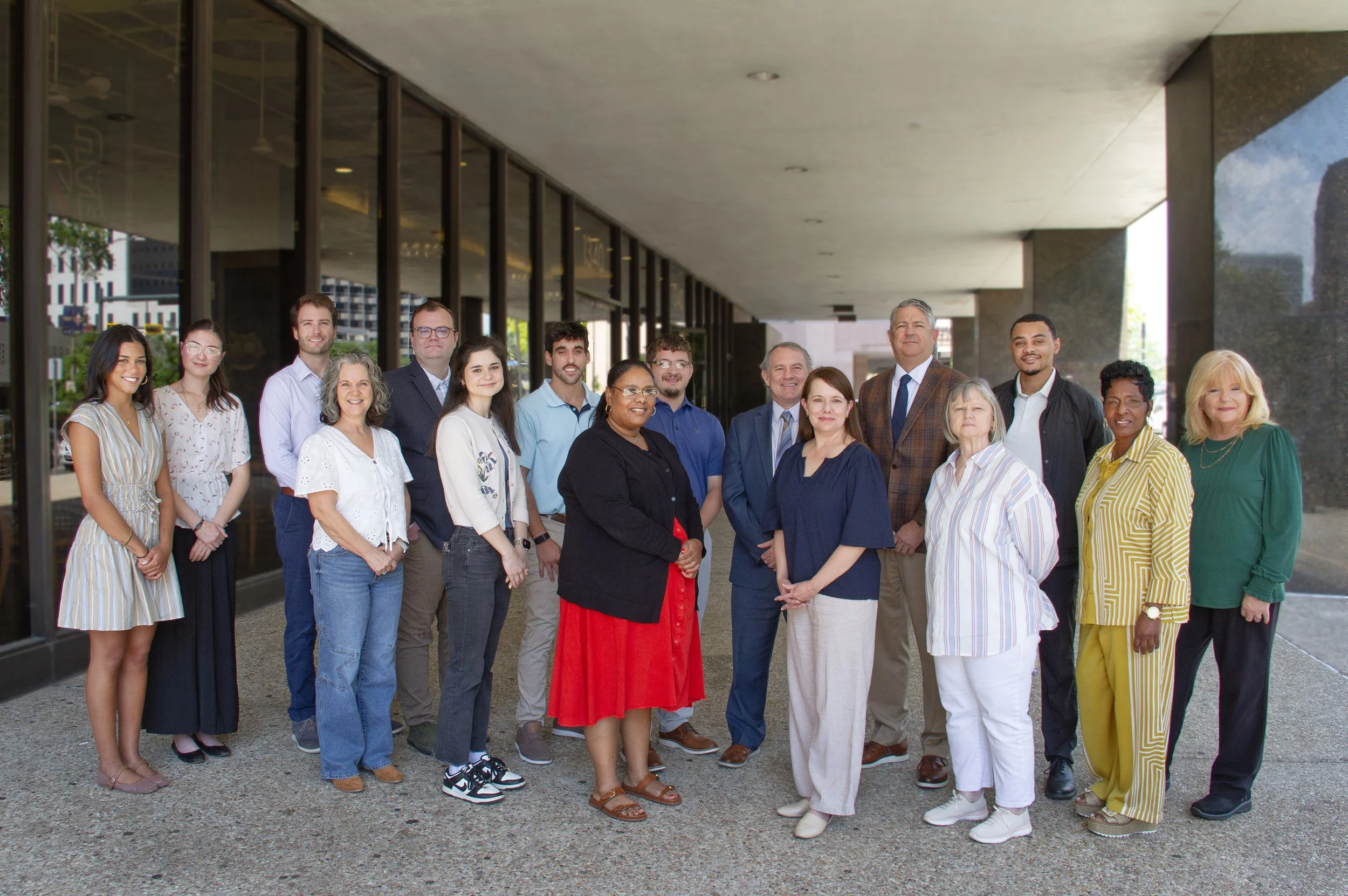 16 people standing together in front of an office building posing for group photo