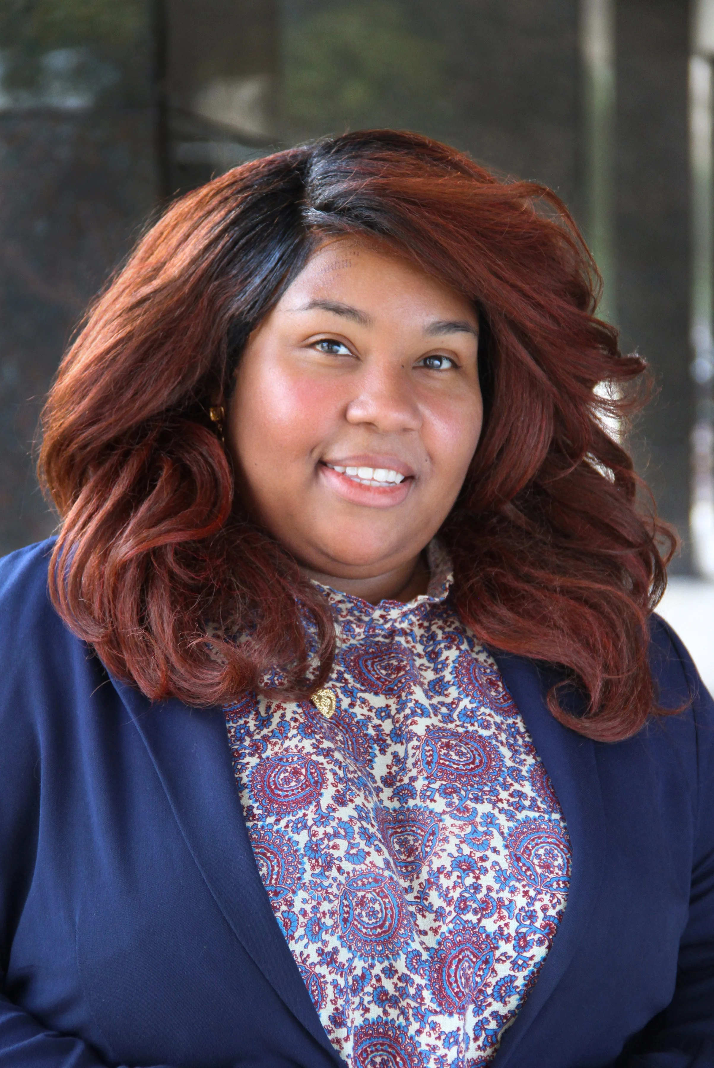 Headshot of woman with long full hair wearing a dark blue jacket over a patterned shirt