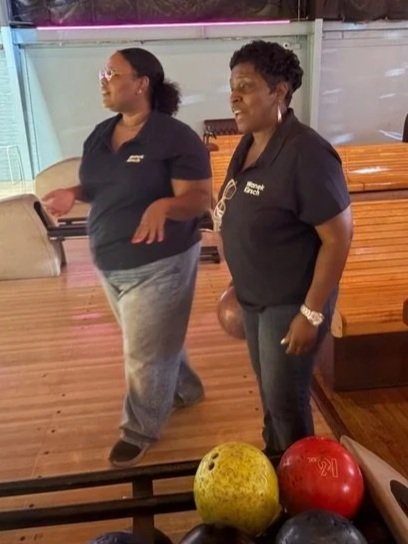 Two woman standing together with one holding a bowling bowl on a bowling lane