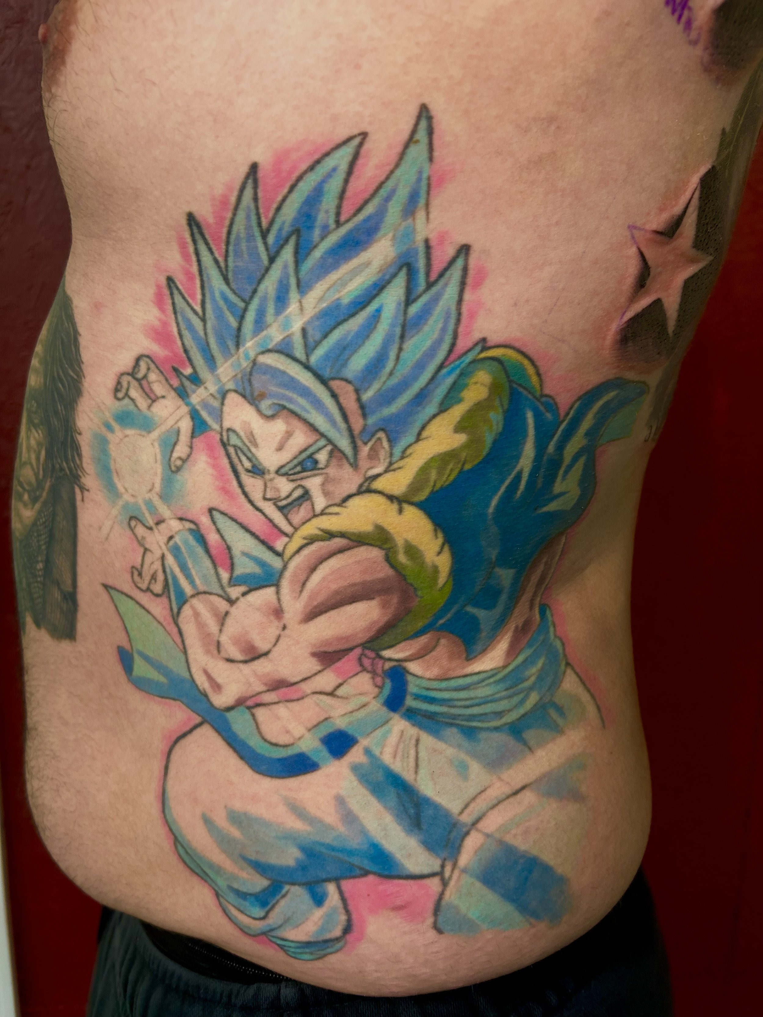 Tattoo of Vegeta with spiky blue hair in a fighting pose, wearing a blue outfit, on a person's side torso by Brett Guerra.