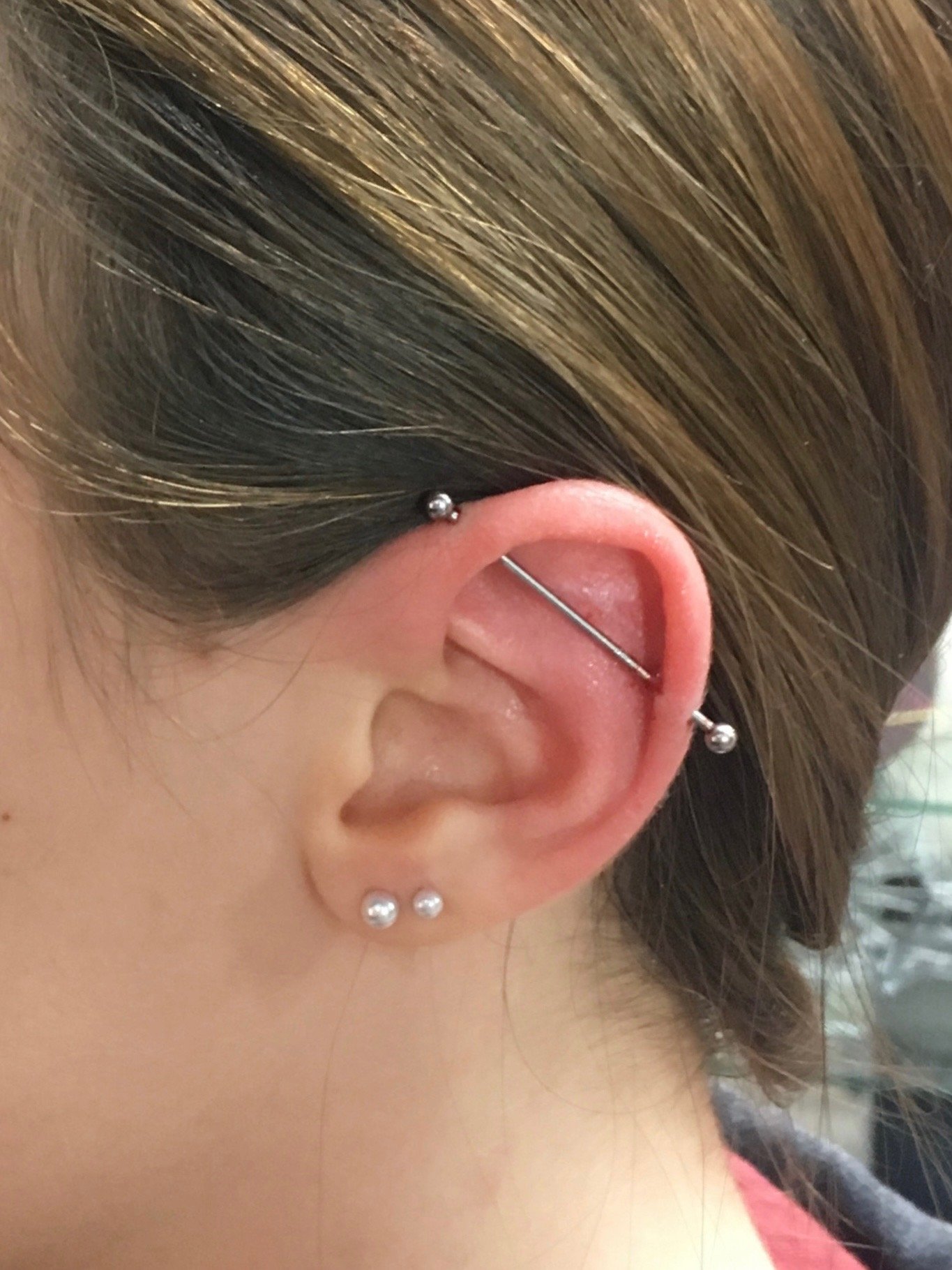 Close-up of a person's ear with an industrial piercing and two lobe piercings with small silver studs.