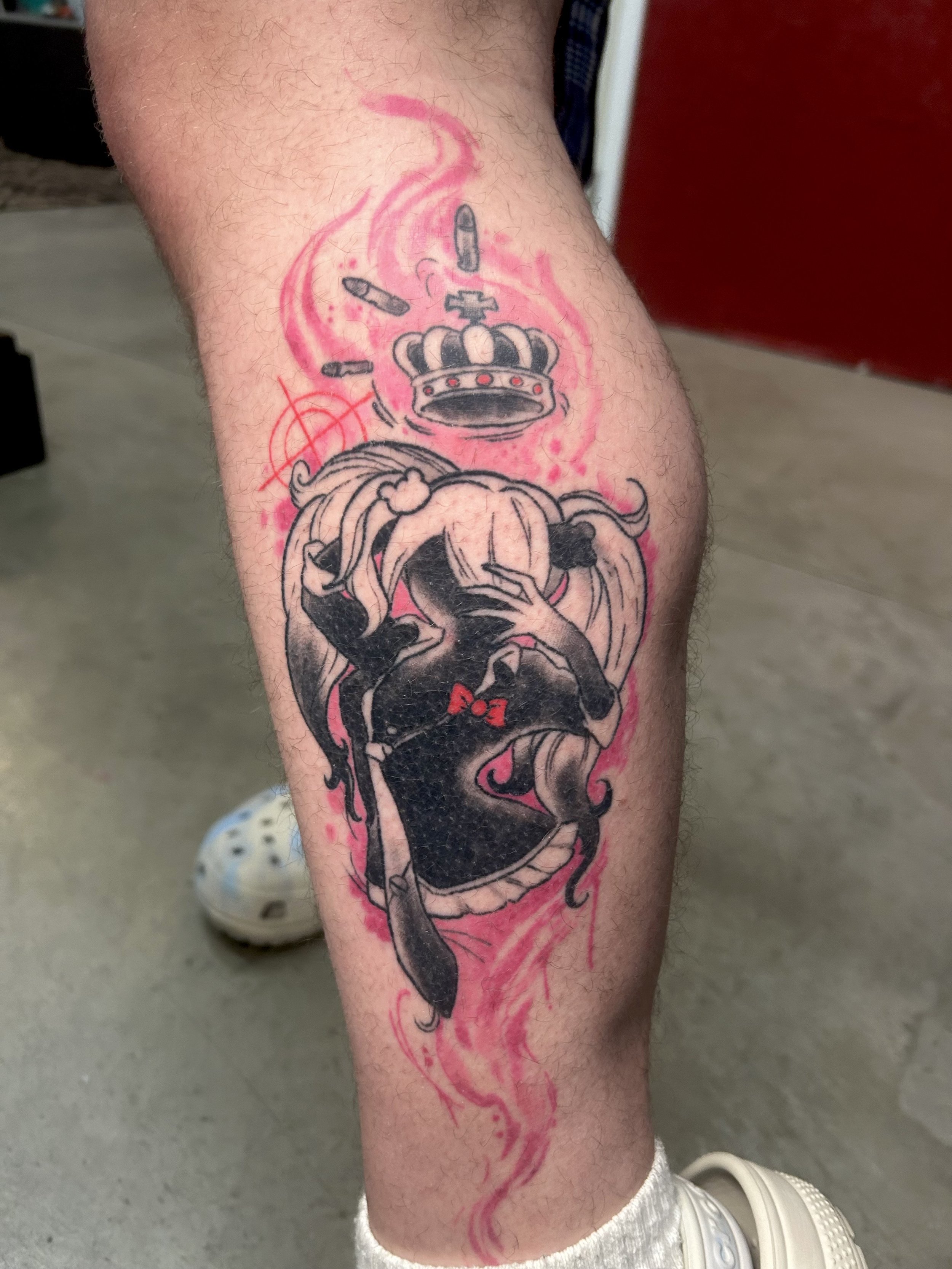 Tattoo featuring a stylized female character with pigtails and a red bow on a leg. Above her is a crown with bullets, surrounded by red swirls and an anarchy symbol by Brett Guerra.