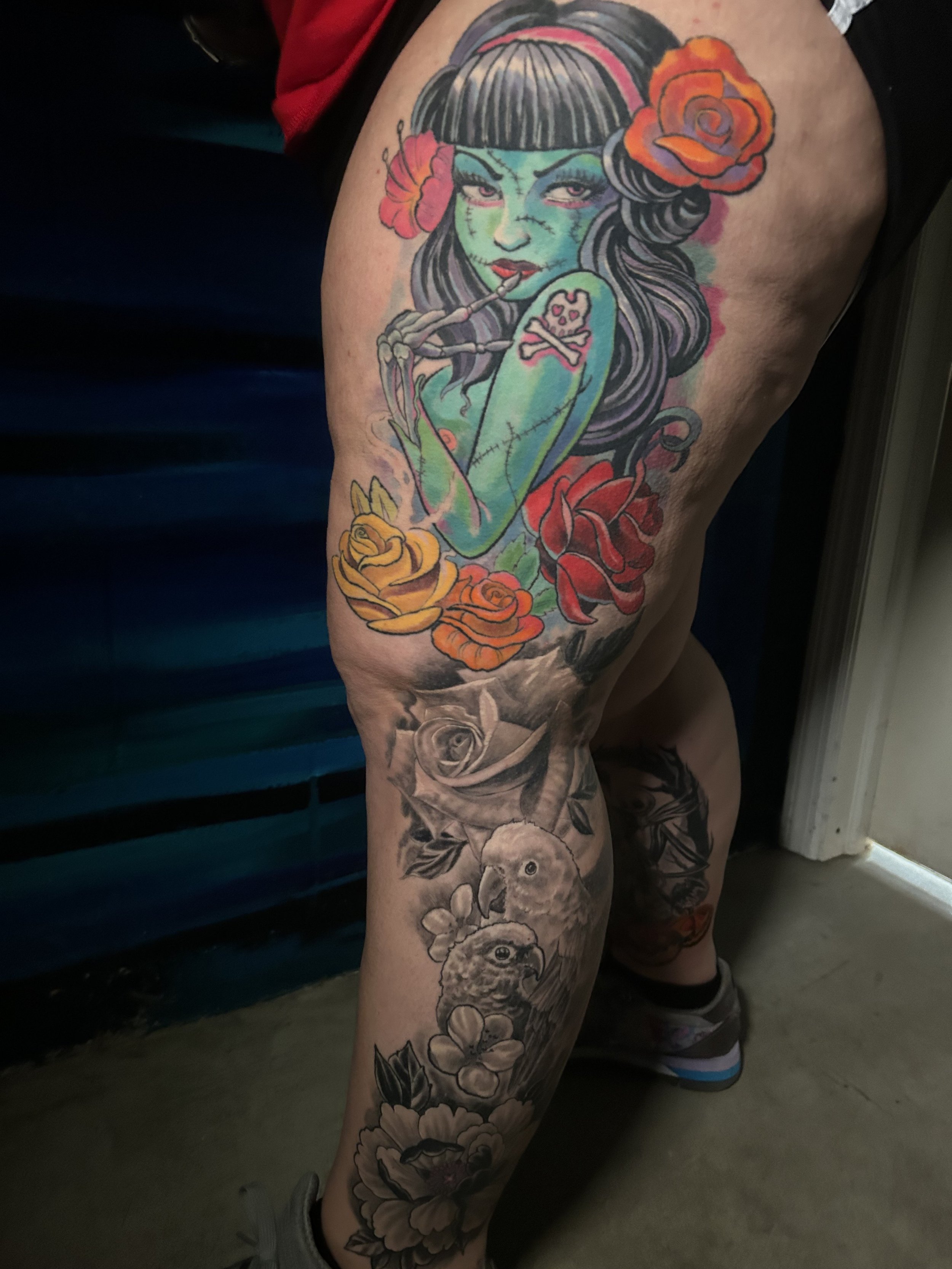 Colorful thigh tattoo featuring a female character with roses, vibrant colors, and black and gray floral pattern with birds. Tattoo by Brett Guerra.