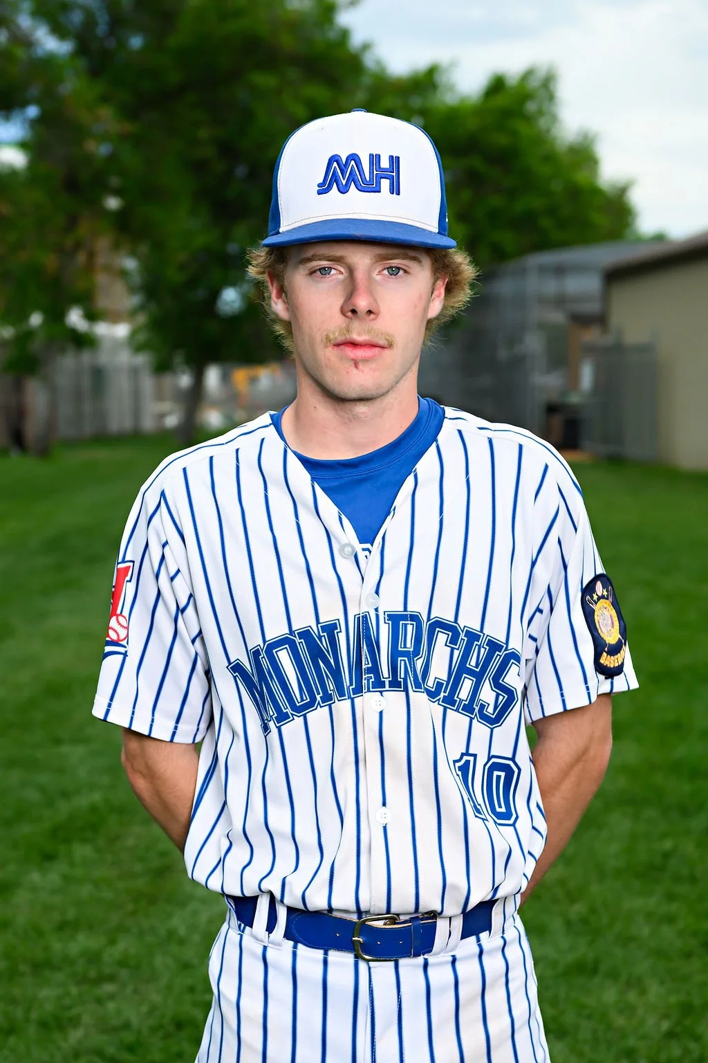 Young baseball player in blue uniform and white cap standing outdoors on a baseball field.
