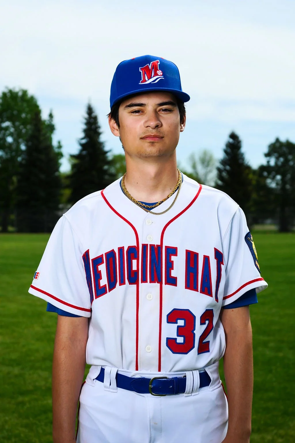 A young male baseball player in a white uniform with red and blue lettering, holding a baseball glove, standing on a baseball field.