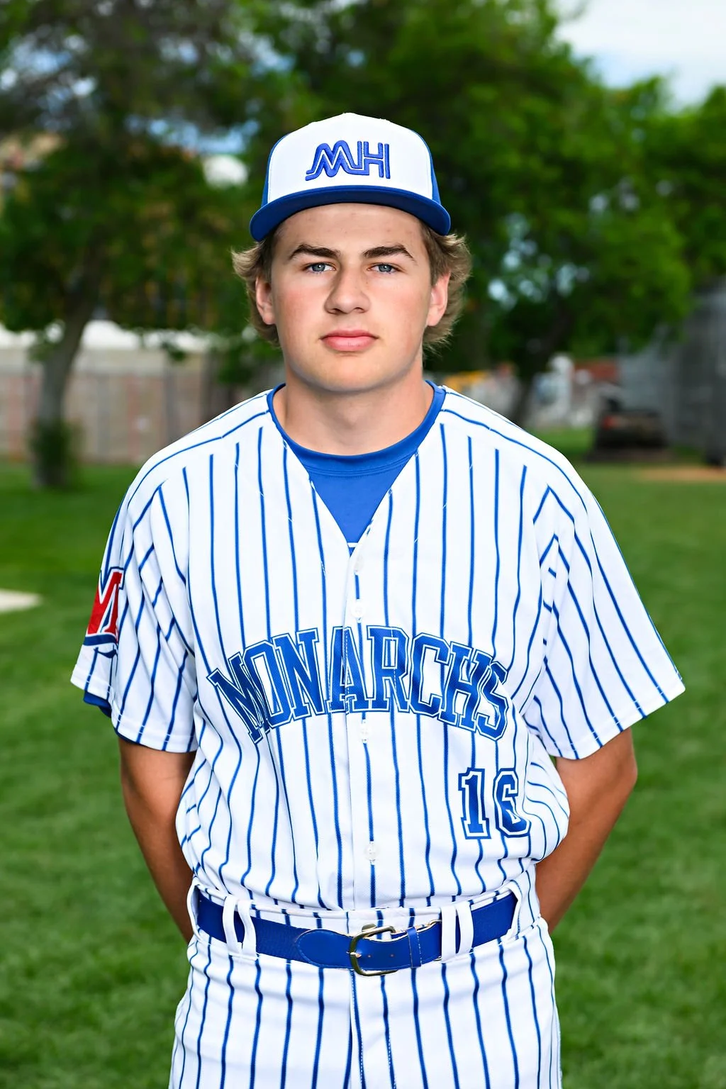 Young man in a blue baseball uniform and cap standing on a baseball field.