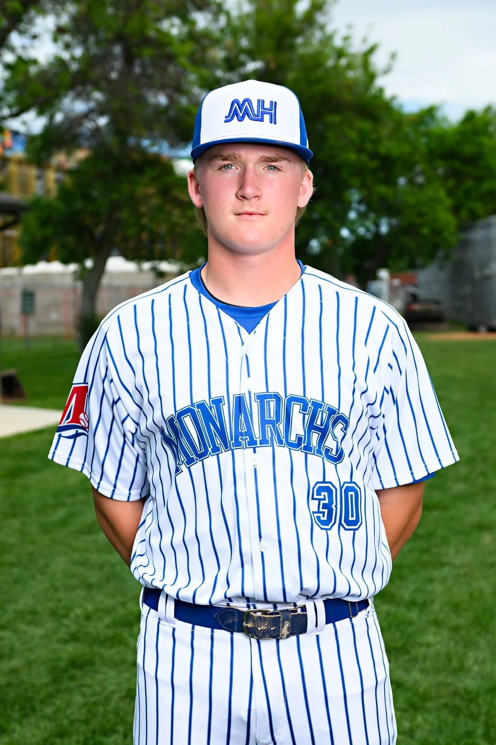 A young male baseball player standing on a baseball field, wearing a blue jersey with the words 'Med Hat' and the number 21, along with a white and blue cap.