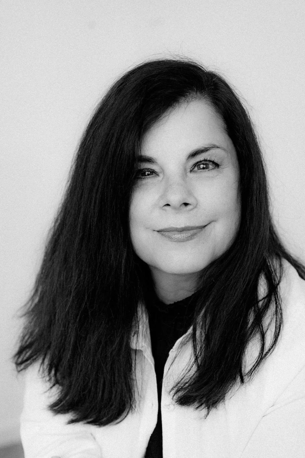 Black and white portrait of a woman with long dark hair, smiling softly, wearing a light-colored top.