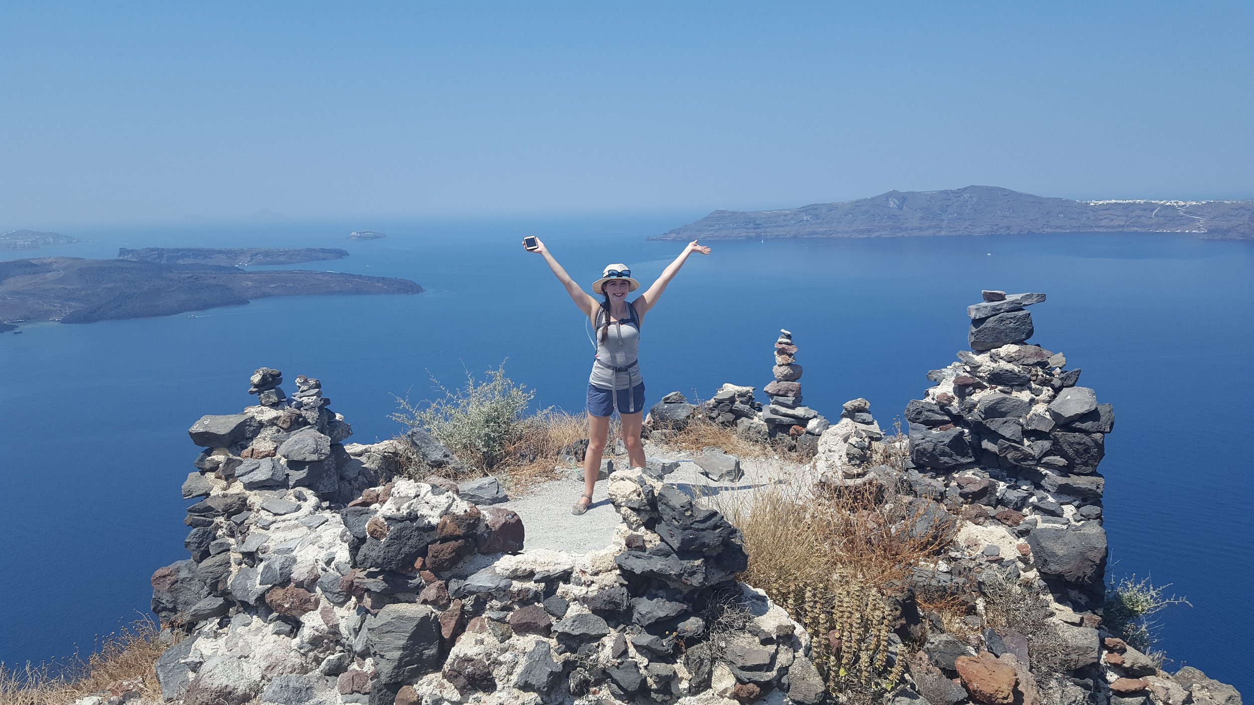 Nick stands in front of the Delicate Arch in Utah looking at his phone. It is winter, the sky is blue and snow is visible in the background.