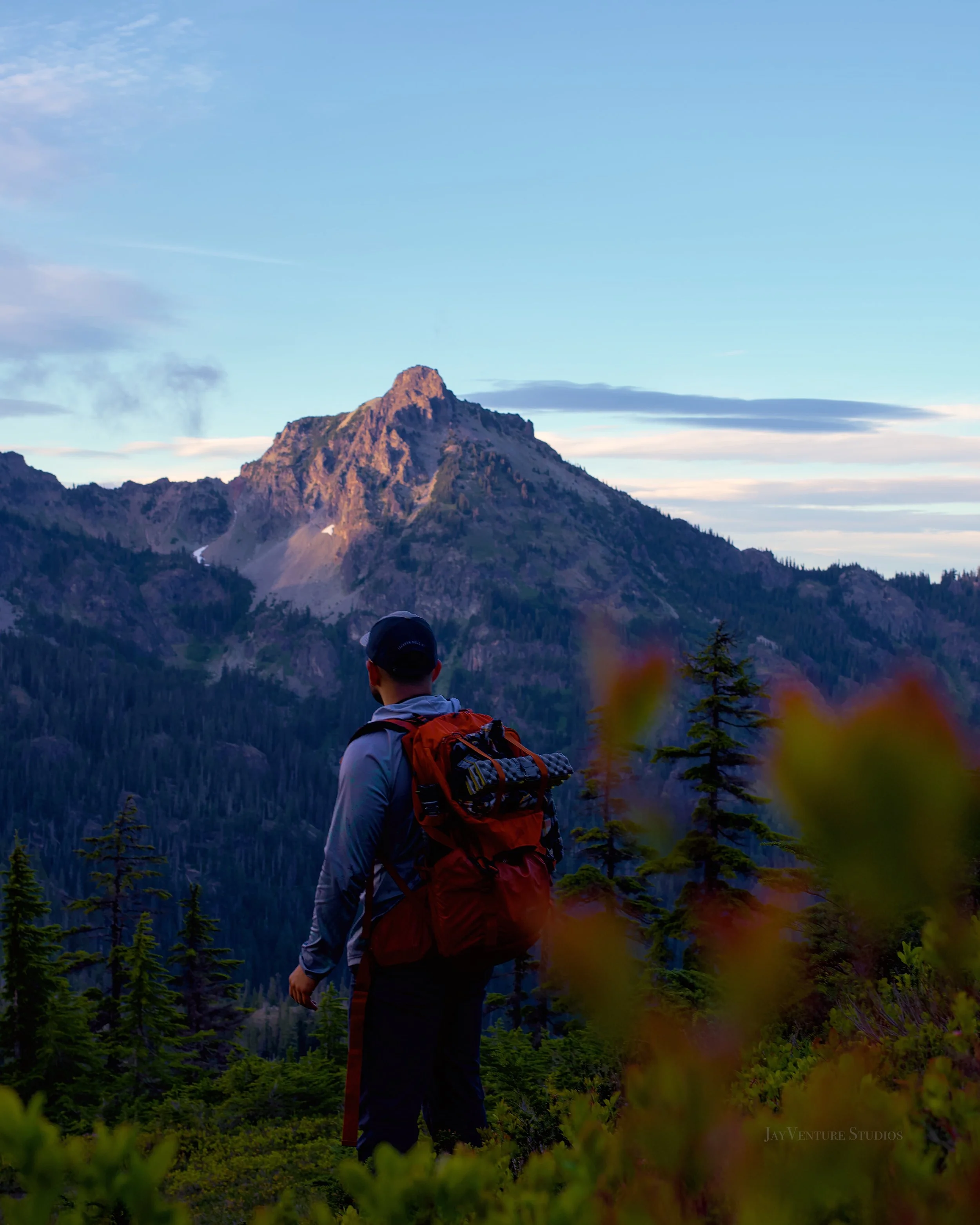 Hiker standing on a mountain trail with a mountain peak in the background under a blue sky during daytime.