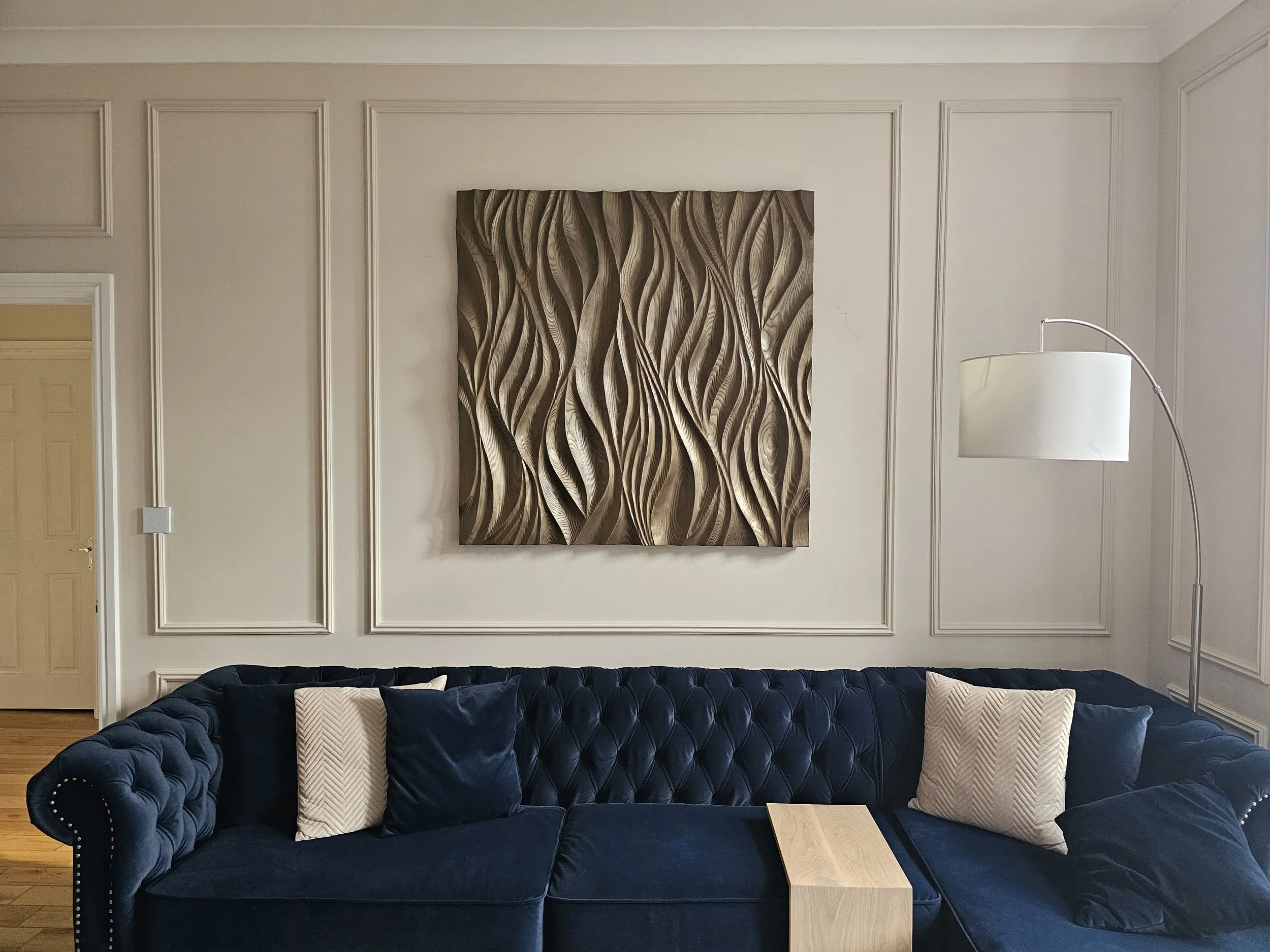 Dreams of Tomorrow, a square carved ash wall panel with flowing waves, hung above a navy sofa