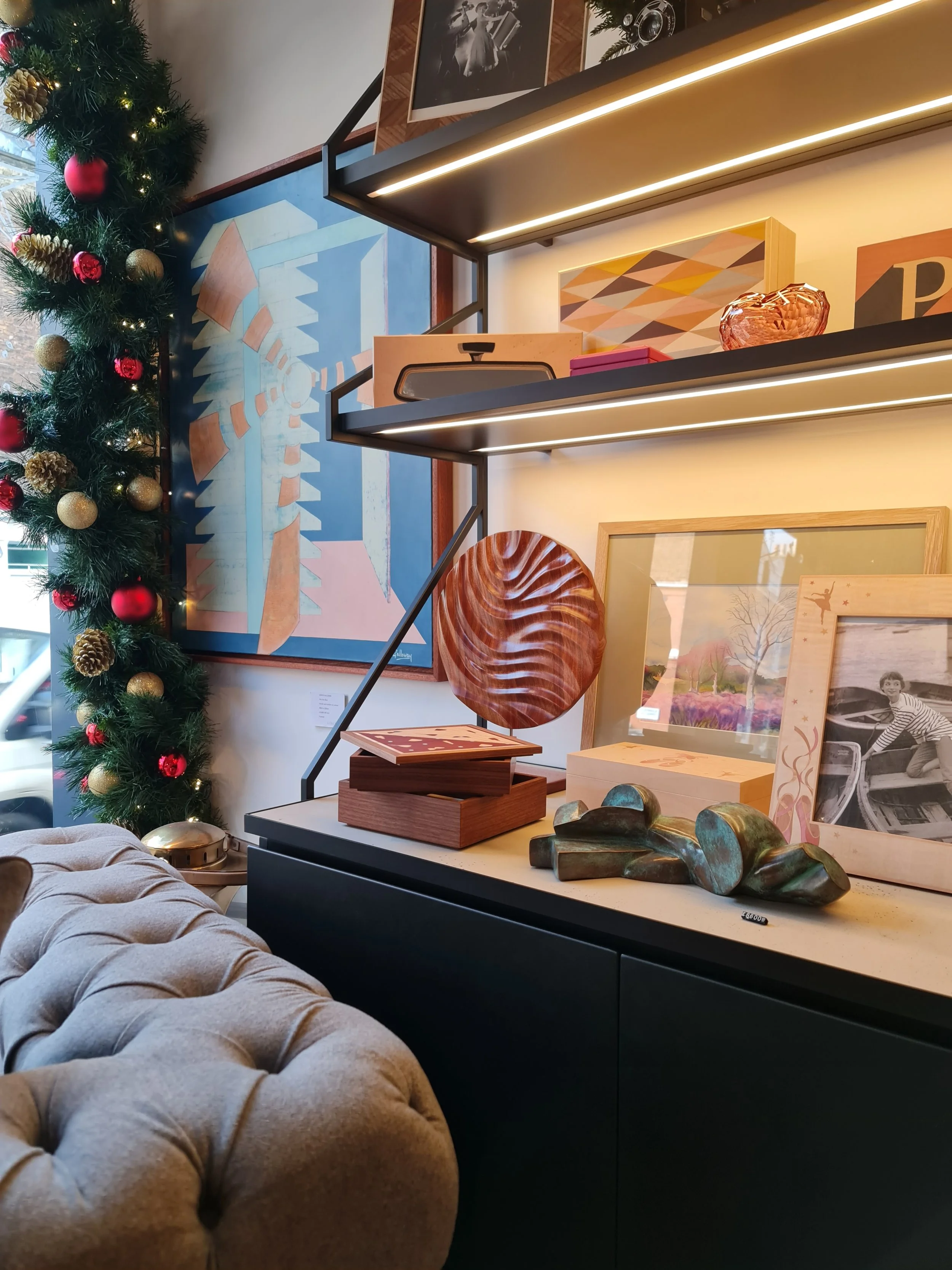 Dancer, a round sapele disc with wave-like ridges, on a stand on a lit gallery shelf