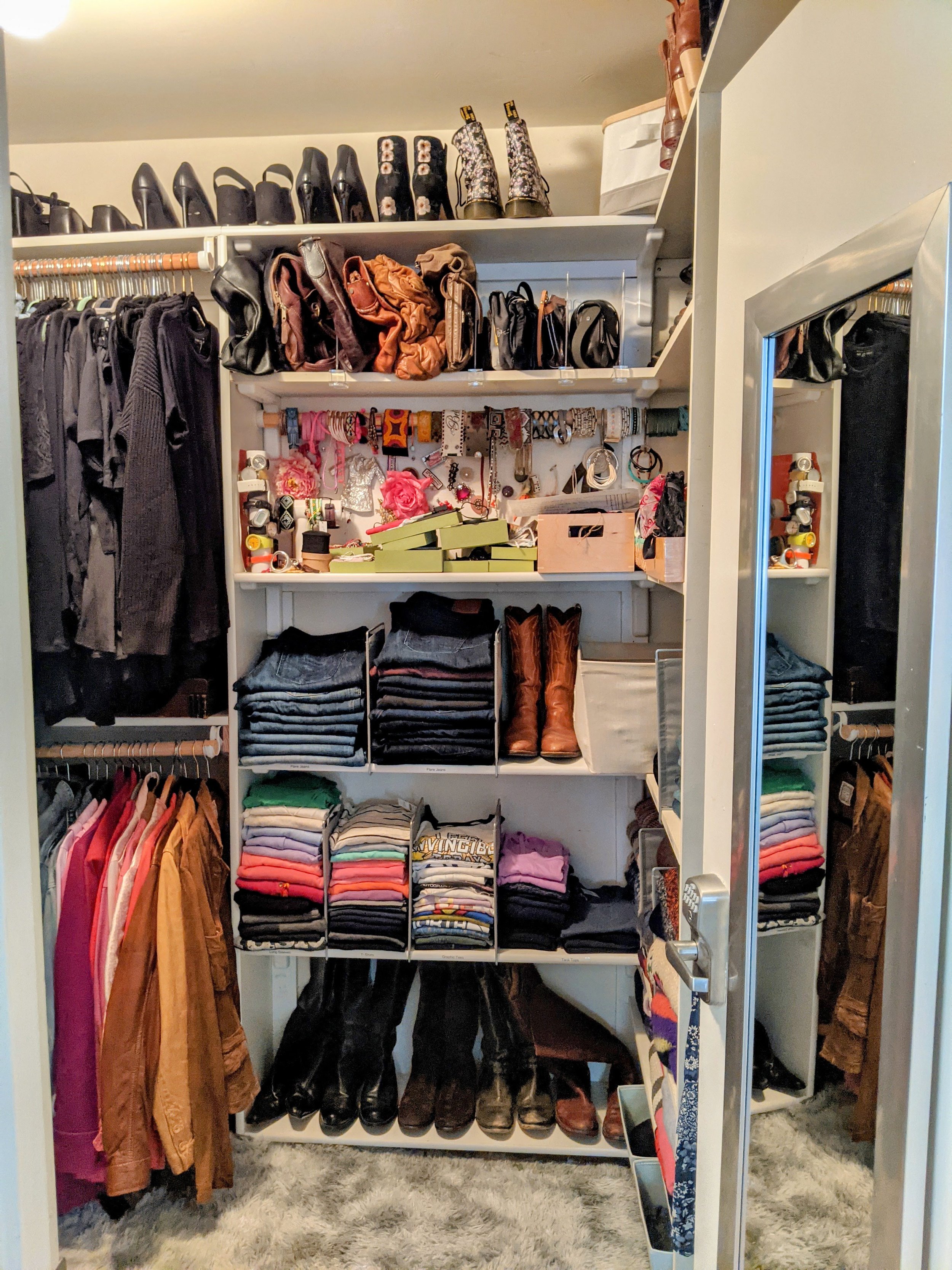 A walk-in closet with shelves full of shoes, handbags, and folded clothes. There are jackets hanging on the left side, and a rug on the floor. The closet has organized storage with various accessories and apparel.