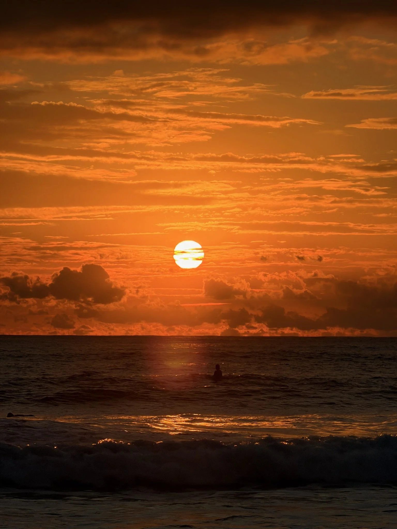 sunset in costa rica. A surfer is seen walking in the ocean.