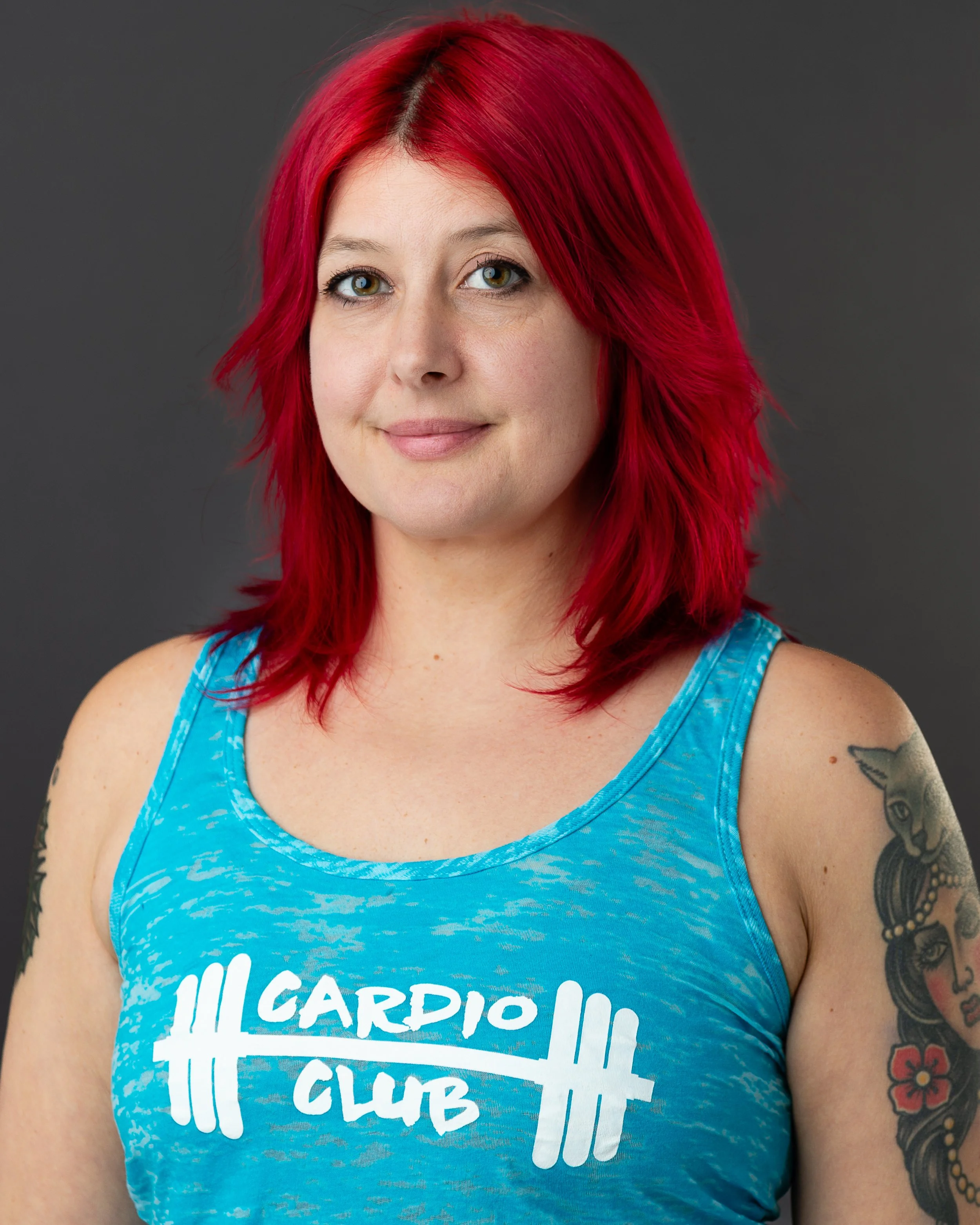 A woman with red hair in a blue long-sleeve shirt and black pants sitting cross-legged on a wooden floor, practicing yoga or meditation in front of a large black and white tapestry featuring celestial and mountain motifs.
