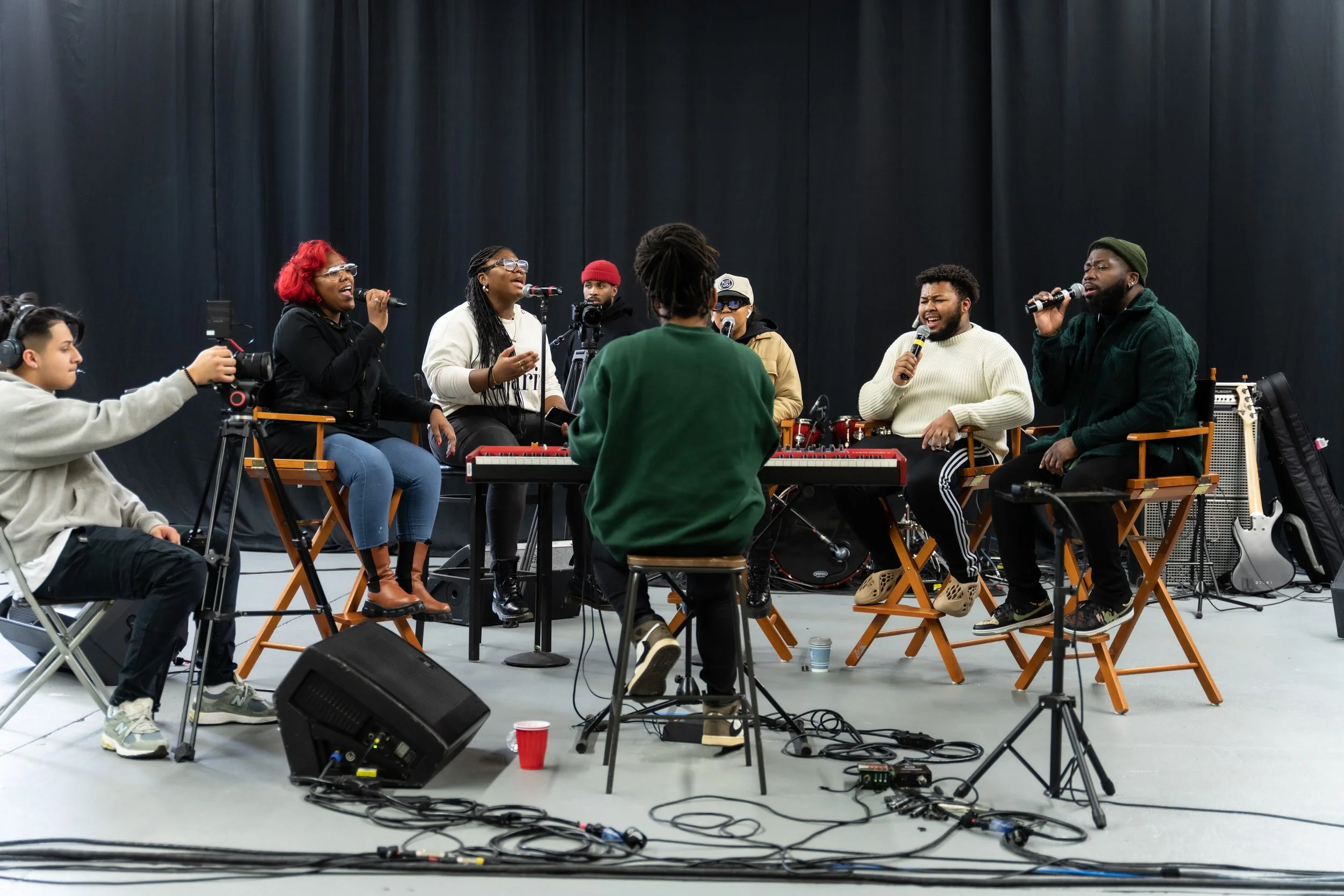Group of people performing and recording music in a studio with musical instruments and microphones.