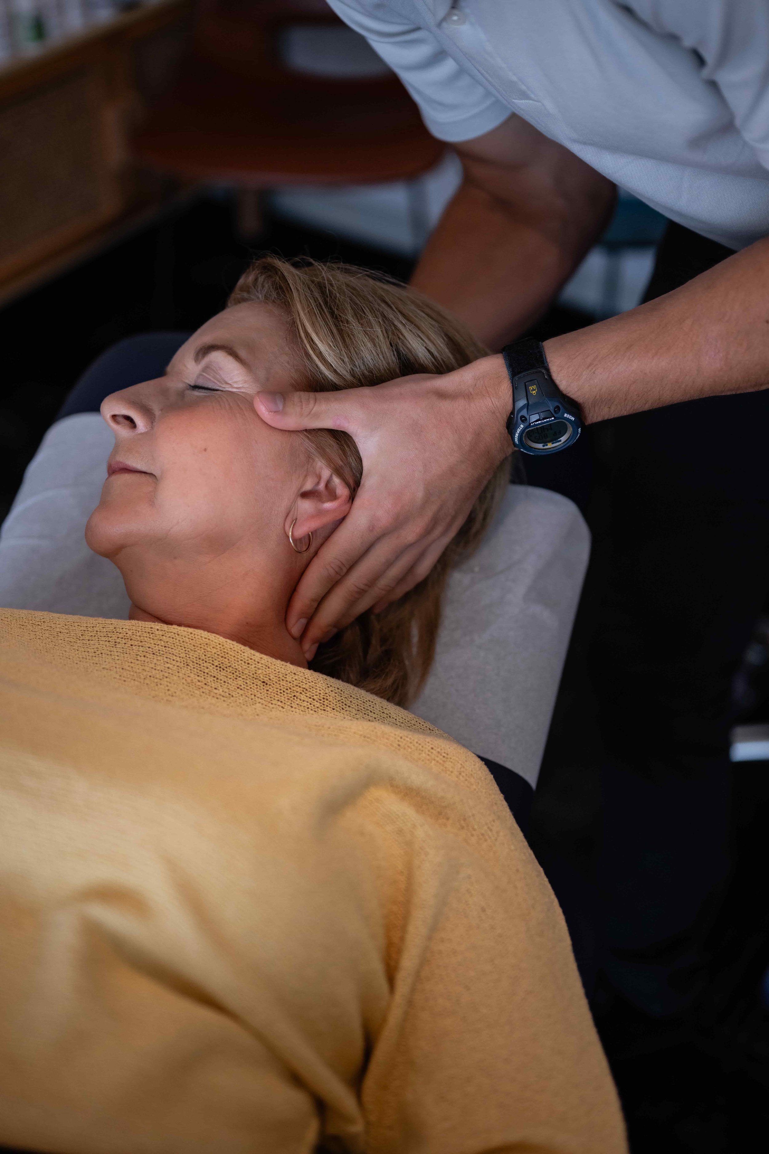 A woman receiving a massage in a spa setting. She has her eyes closed and appears relaxed. The massage therapist is applying pressure to her neck and head area.