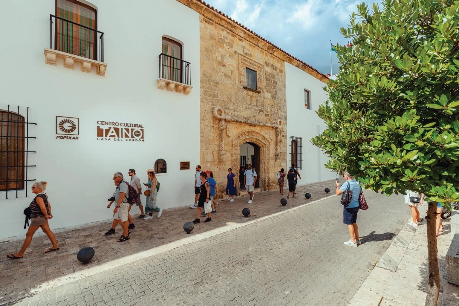 Exterior of Centro Cultural Taíno Casa del Cordón featuring its historic stone portal and white facade with tourists walking by in Zona Colonial Santo Domingo.