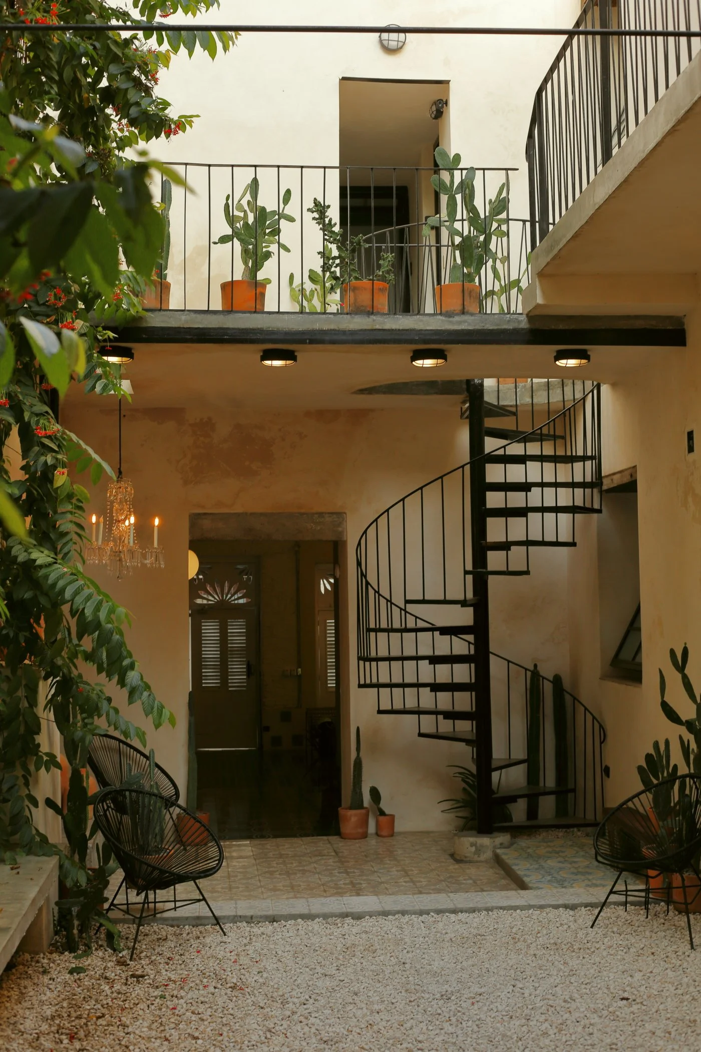 Inner courtyard of a modern building with potted cacti and plants, spiral staircase, and outdoor lighting.