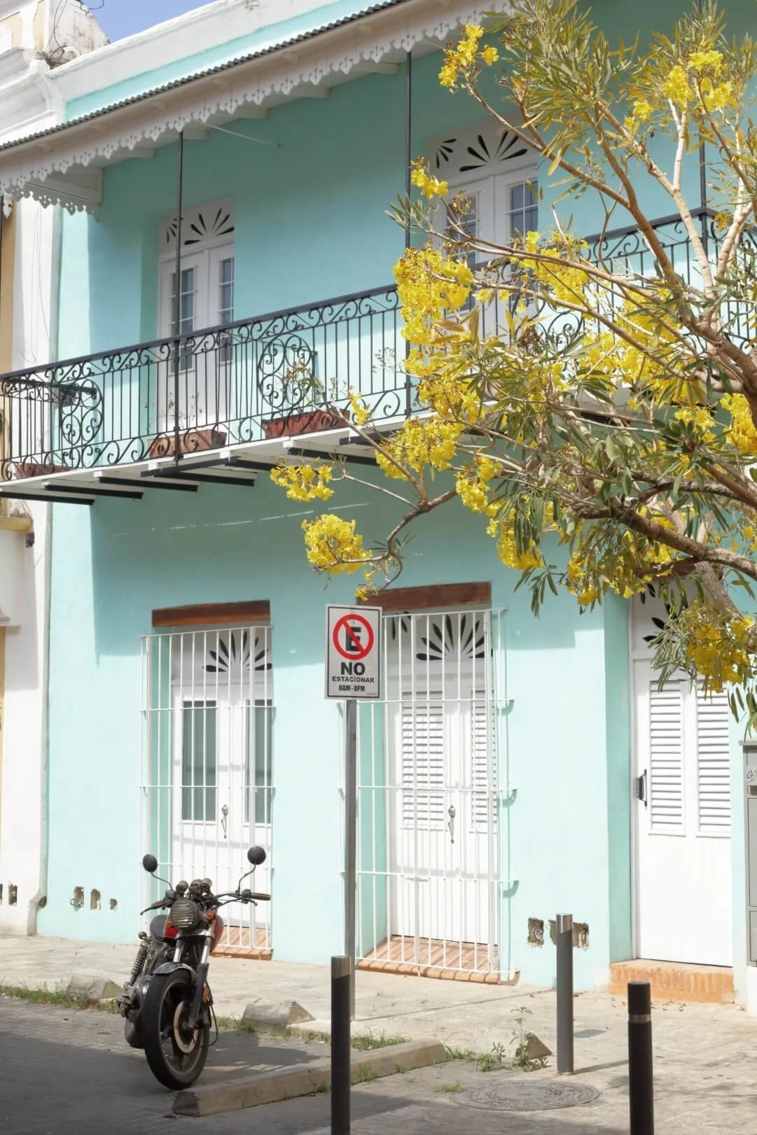 Mint blue colonial house with a black wrought iron balcony and yellow flowering tree in Zona Colonial Santo Domingo.