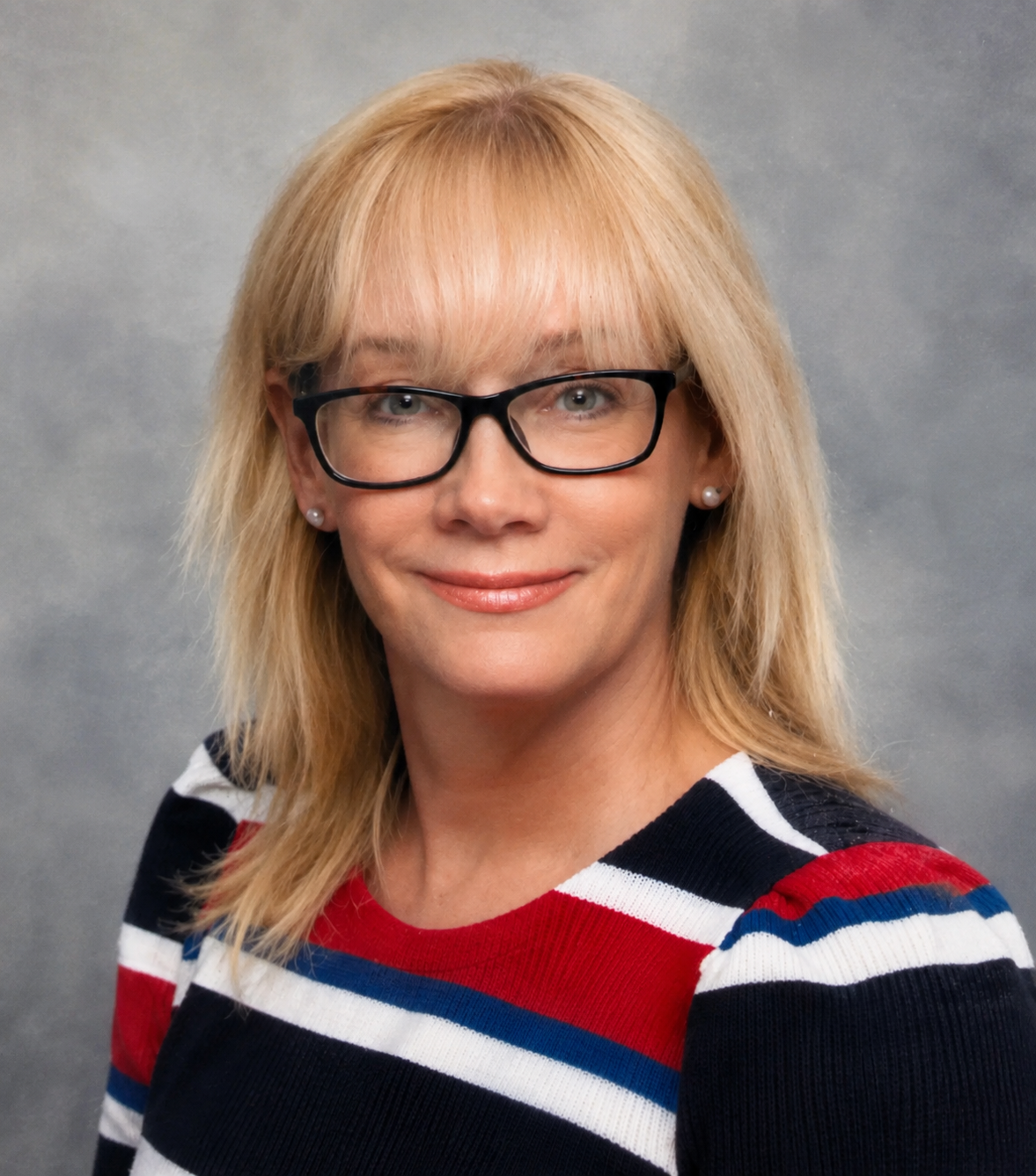 A woman with blonde hair, wearing glasses, a colorful striped sweater, and earrings, smiling at the camera.