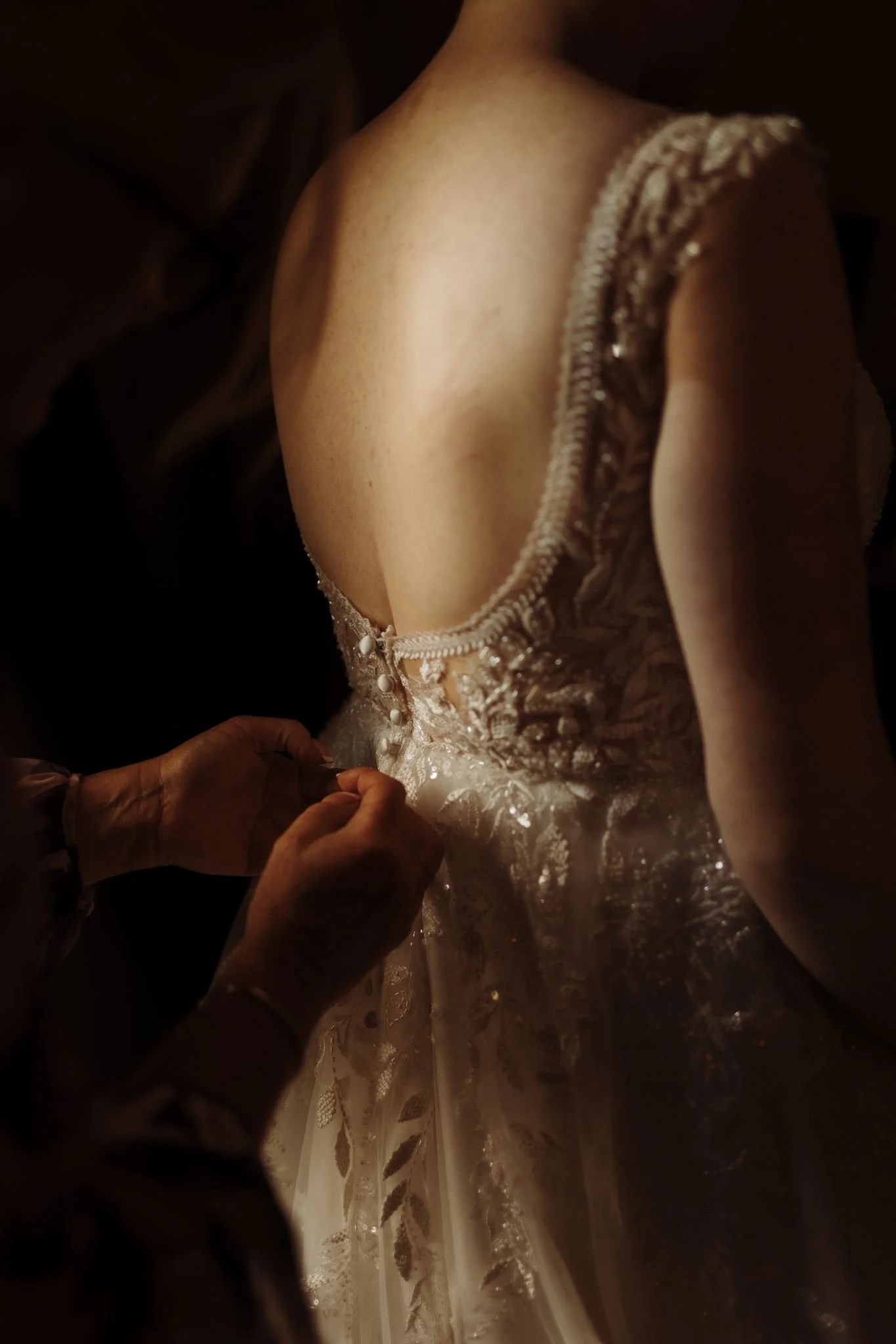 A person adjusting the back of a wedding dress with intricate lace and bead details