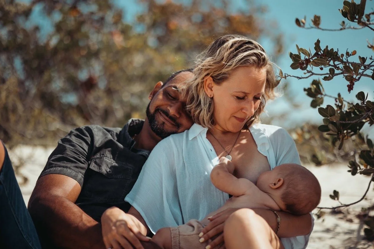 A family hugging on a beach while a mother looks gently down at her child.
