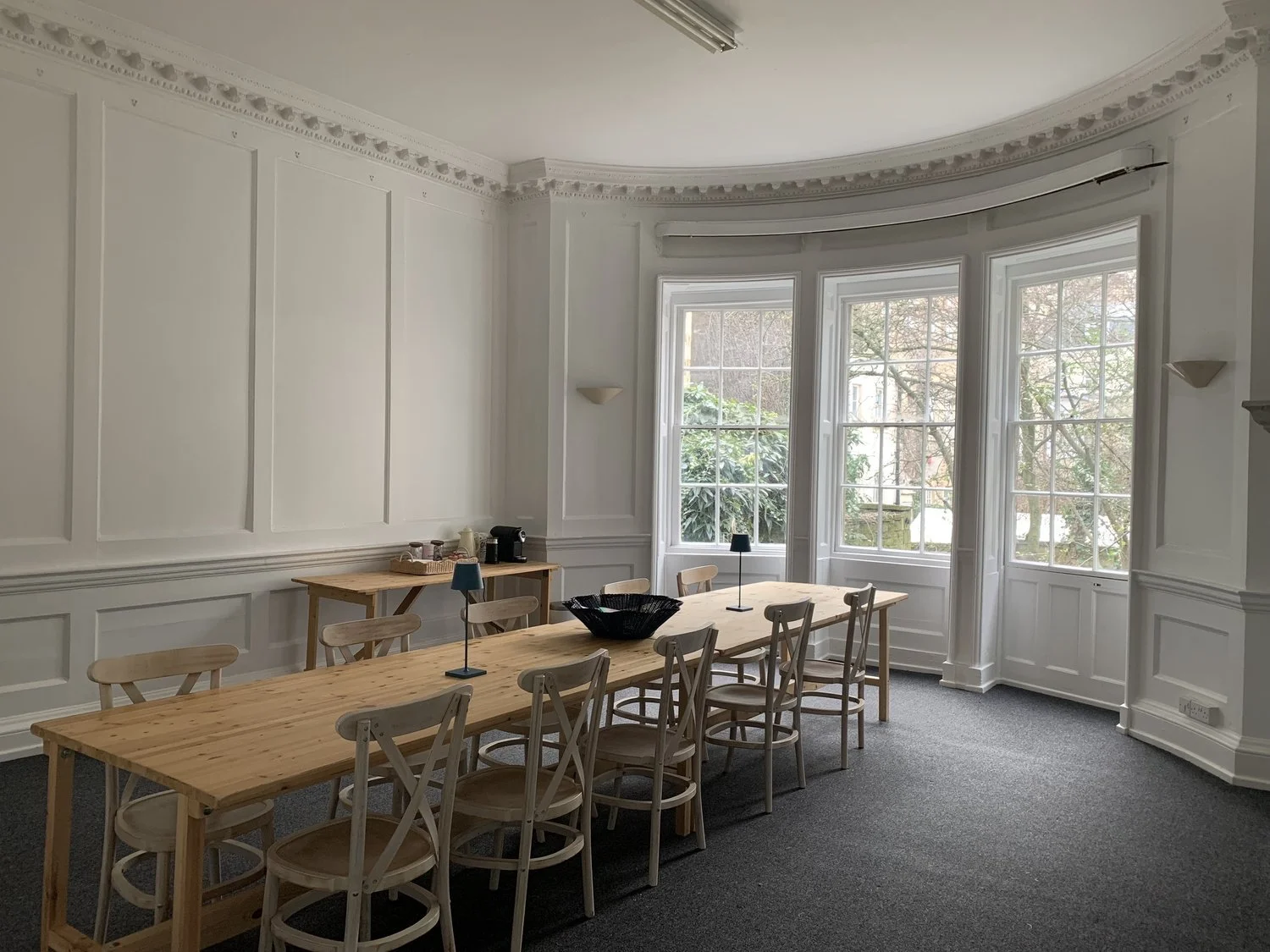 Spacious room with long wooden table and chairs, large windows, and minimal decor.