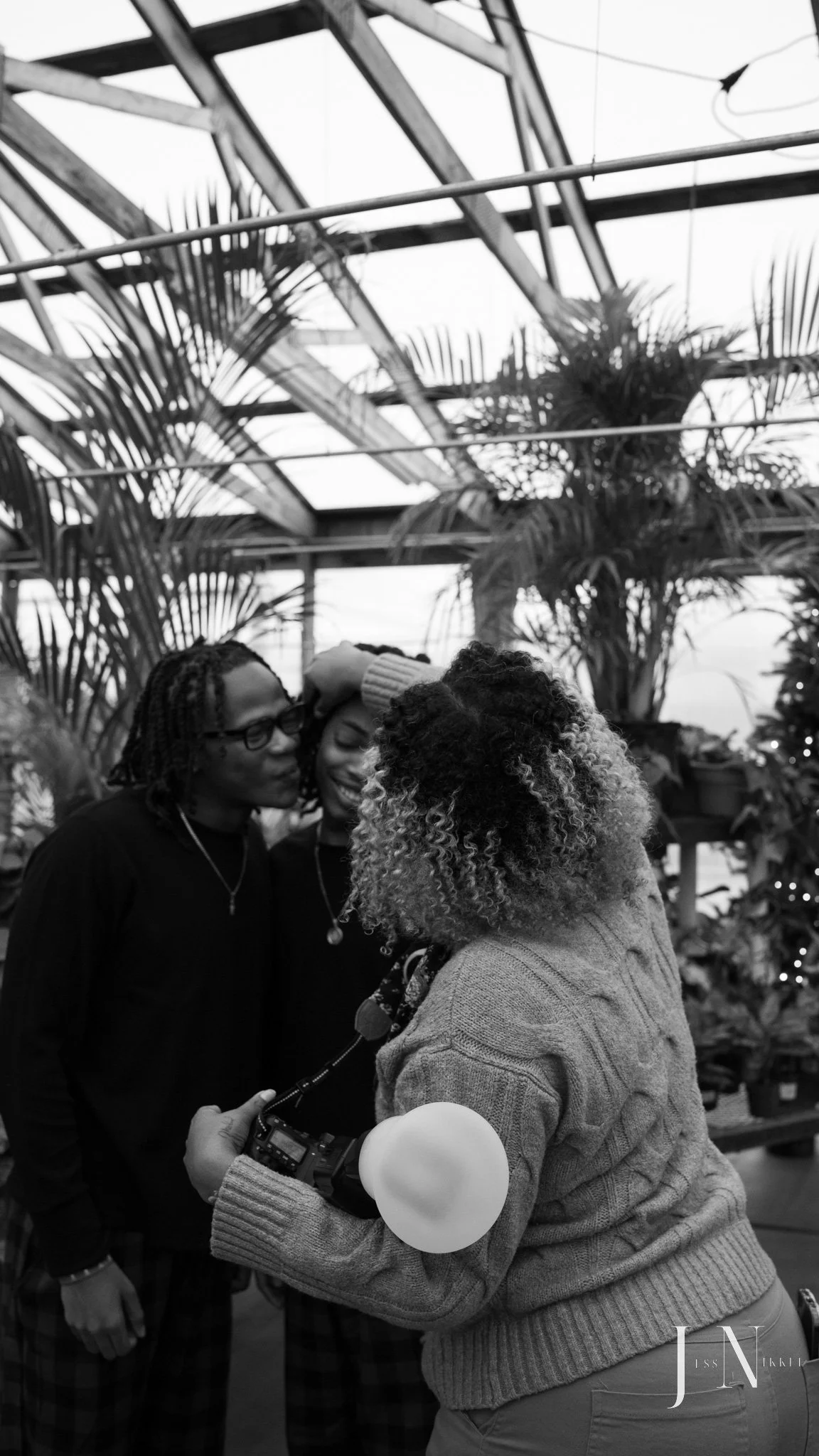 photographer adjusting hair of clients in greenhouse, black and white photo