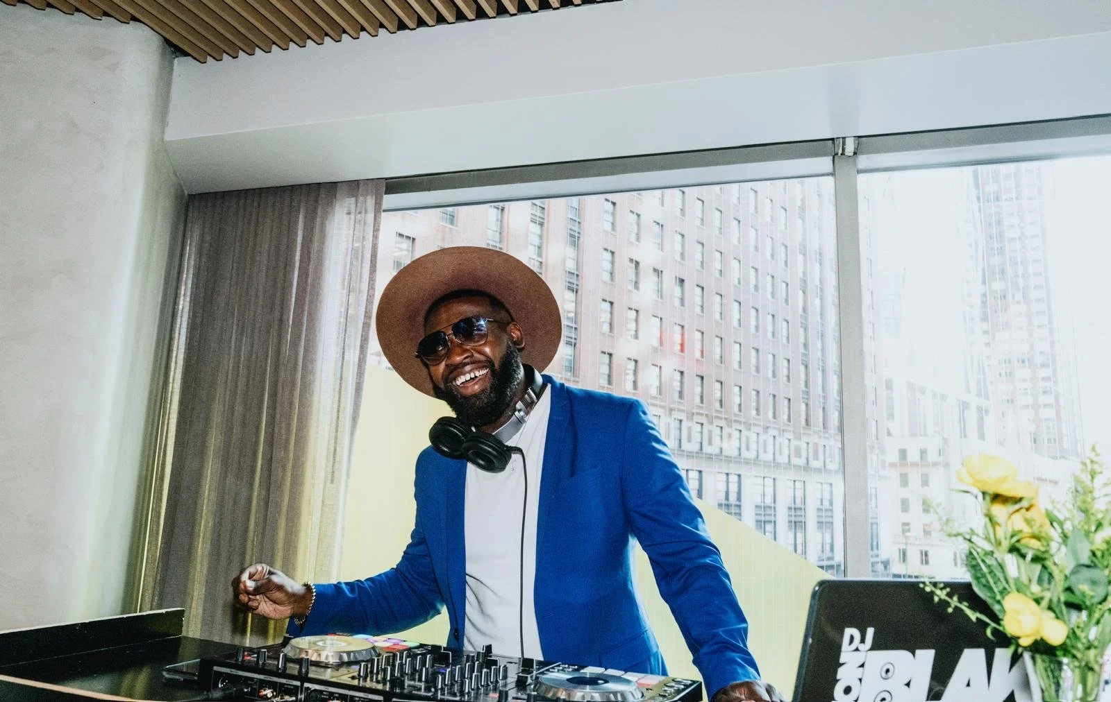 “NYC Wedding DJ & MC DJ Jon Blak smiling while performing at a modern indoor venue, delivering professional DJ services for weddings, corporate events, and sports events in New York City.”