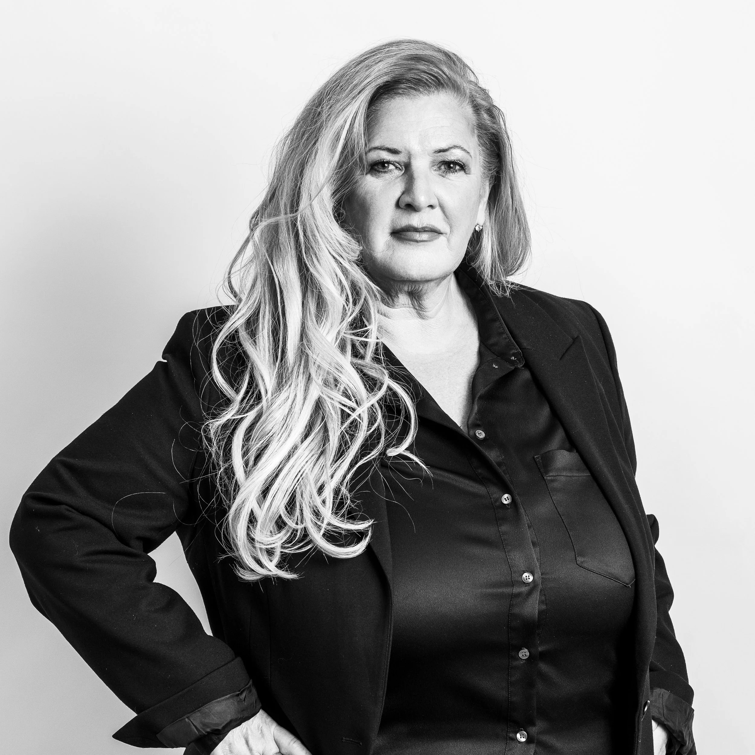 Black and white portrait of a woman with long, wavy hair, wearing a dark blazer and a light shirt against a plain background.
