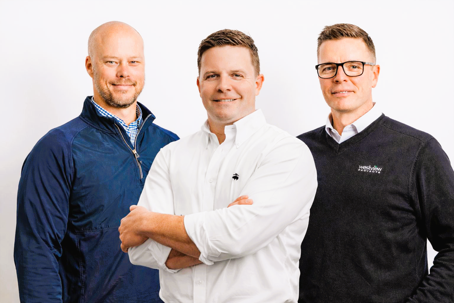 Three professional men standing together against a white background, dressed in business casual attire, smiling at the camera.