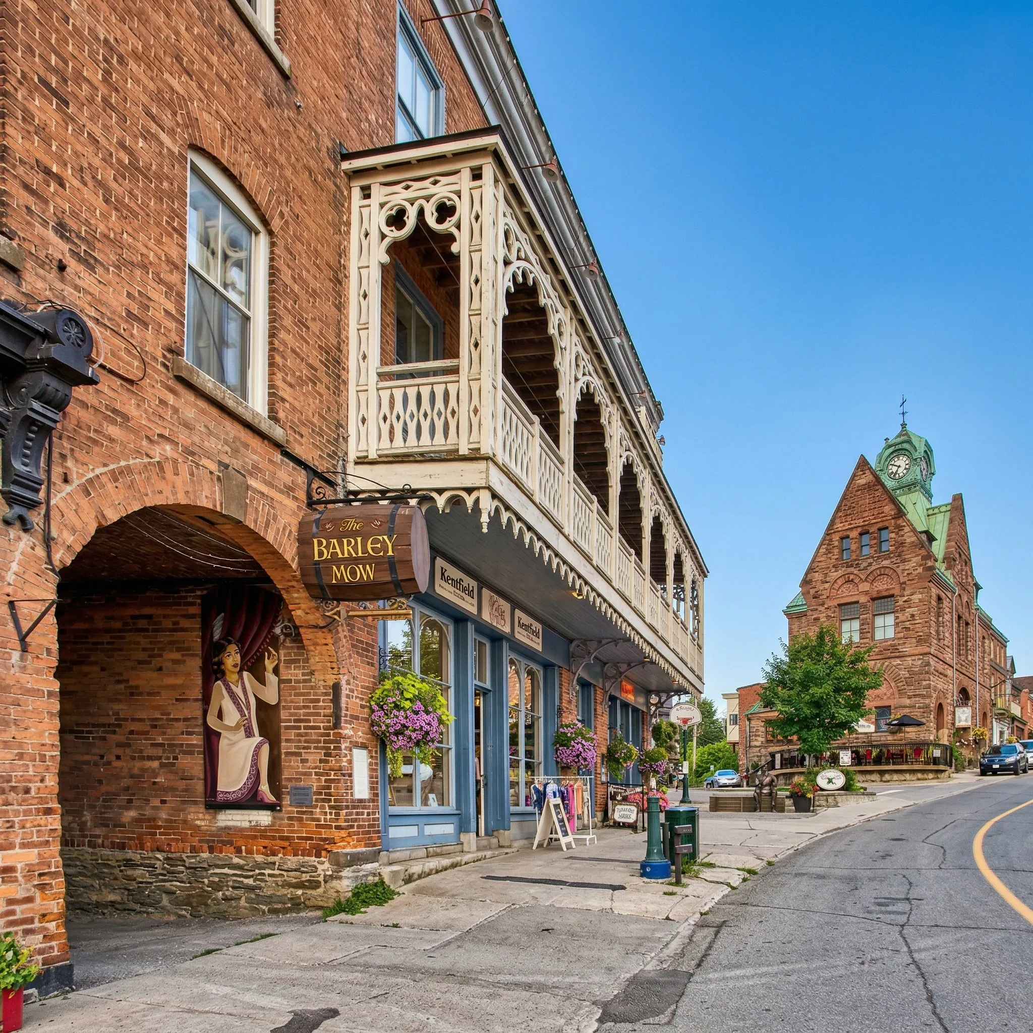 Street view of a historic brick building with a decorative white wooden balcony, flower pots, and merchandise displays, under a clear blue sky.