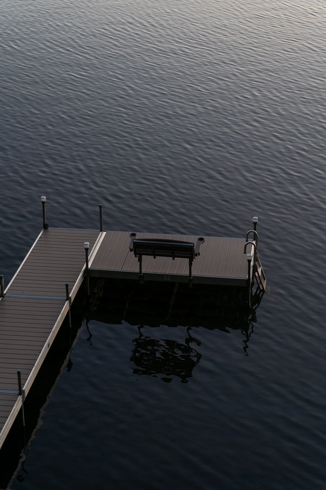 A wooden dock extends over calm water, with a bench and steps at the end of the dock, and reflections visible on the water surface. Located in East Hampton, CT.