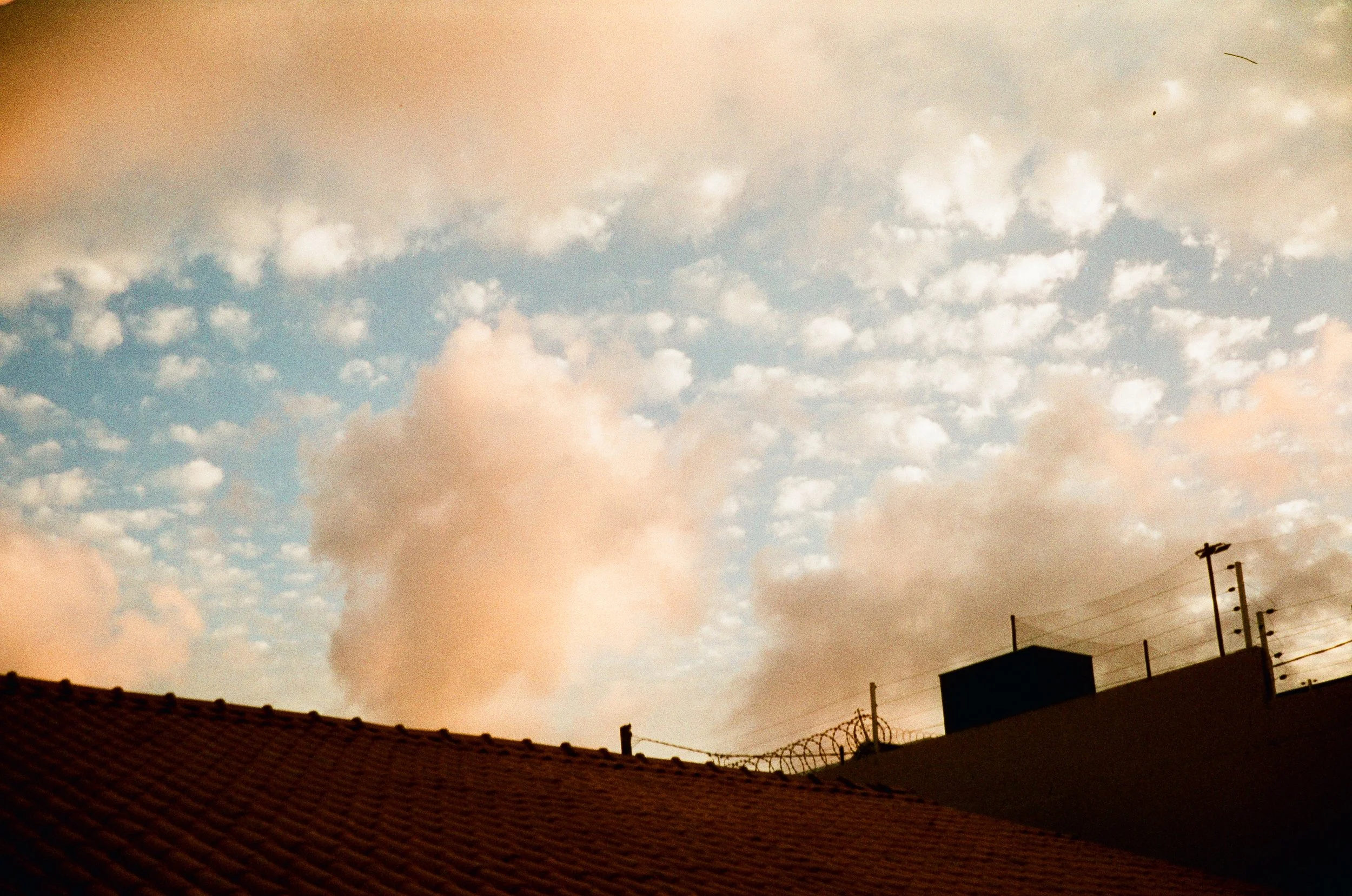 Cloudy sky during sunset above rooftops with a barbed wire fence, located in Fortaleza, Ceará, Brazil.